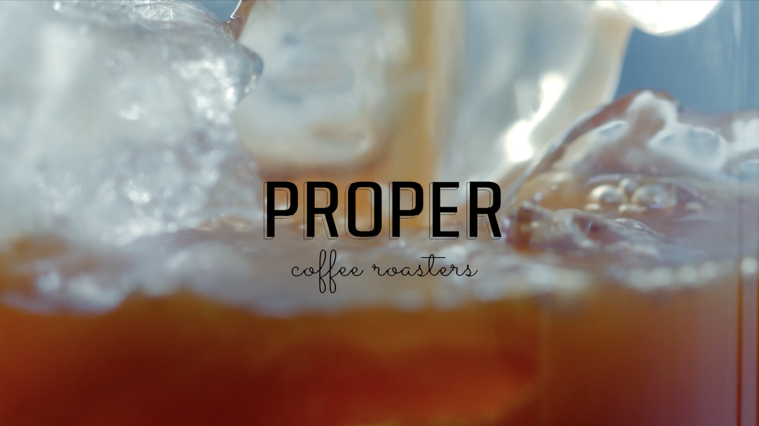 Close-up of coffee being poured over ice with the text 'Proper coffee roasters' overlaid.