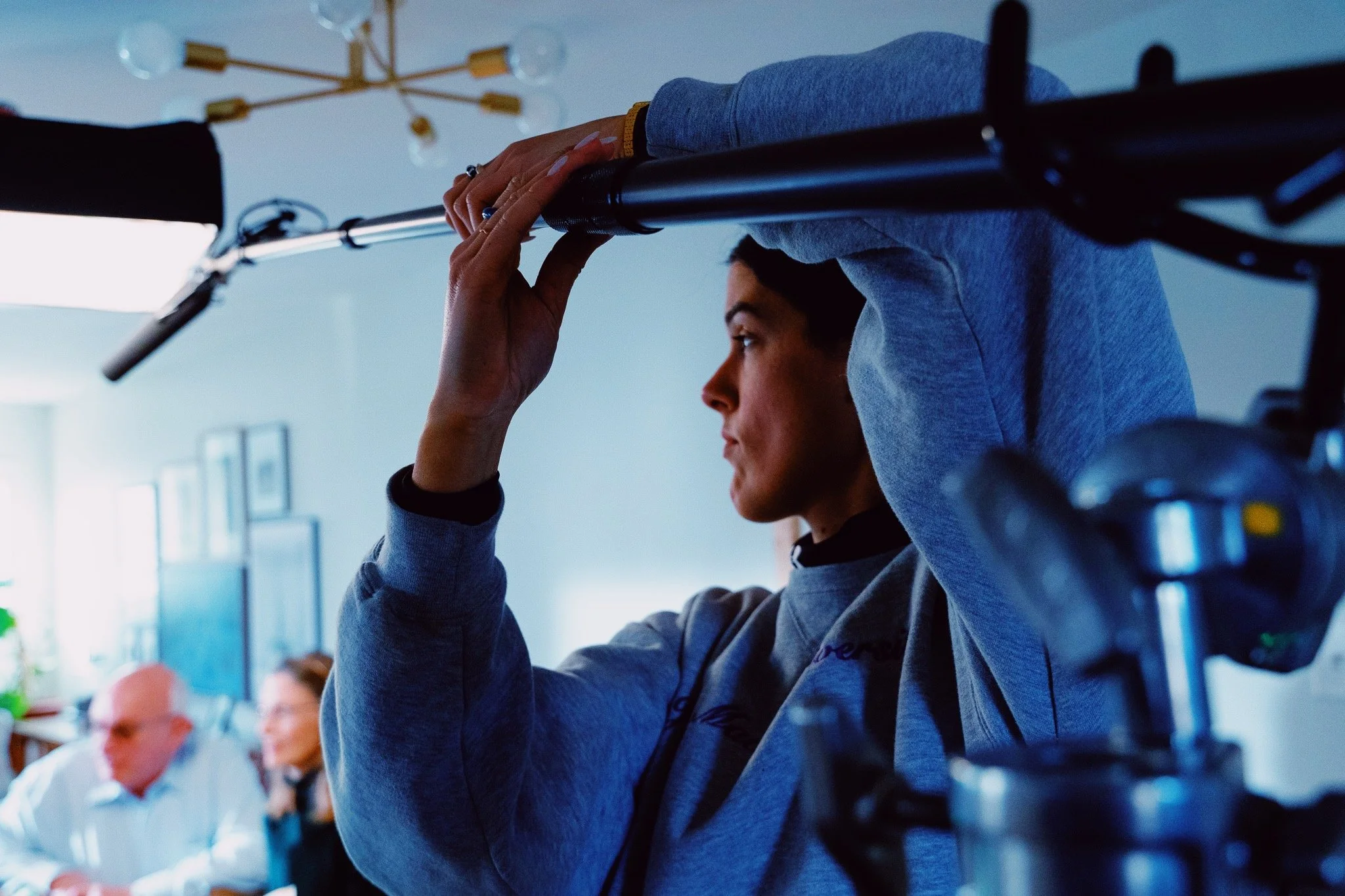 A femail adjusting a boom microphone for video production in an indoor setting.