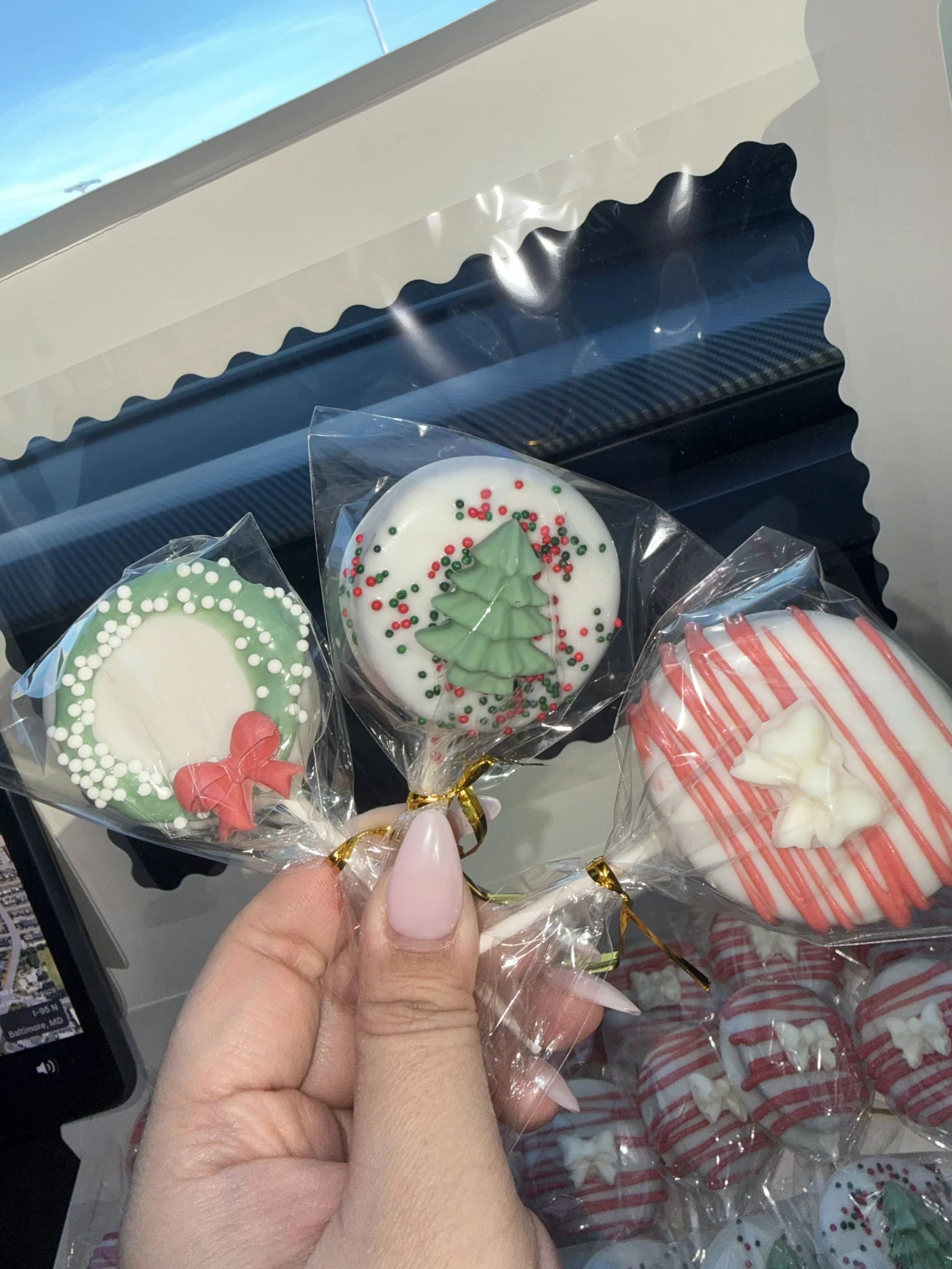 Hand holding three Christmas-themed decorated cookies in clear plastic wrapping, with a snack vending machine in the background.