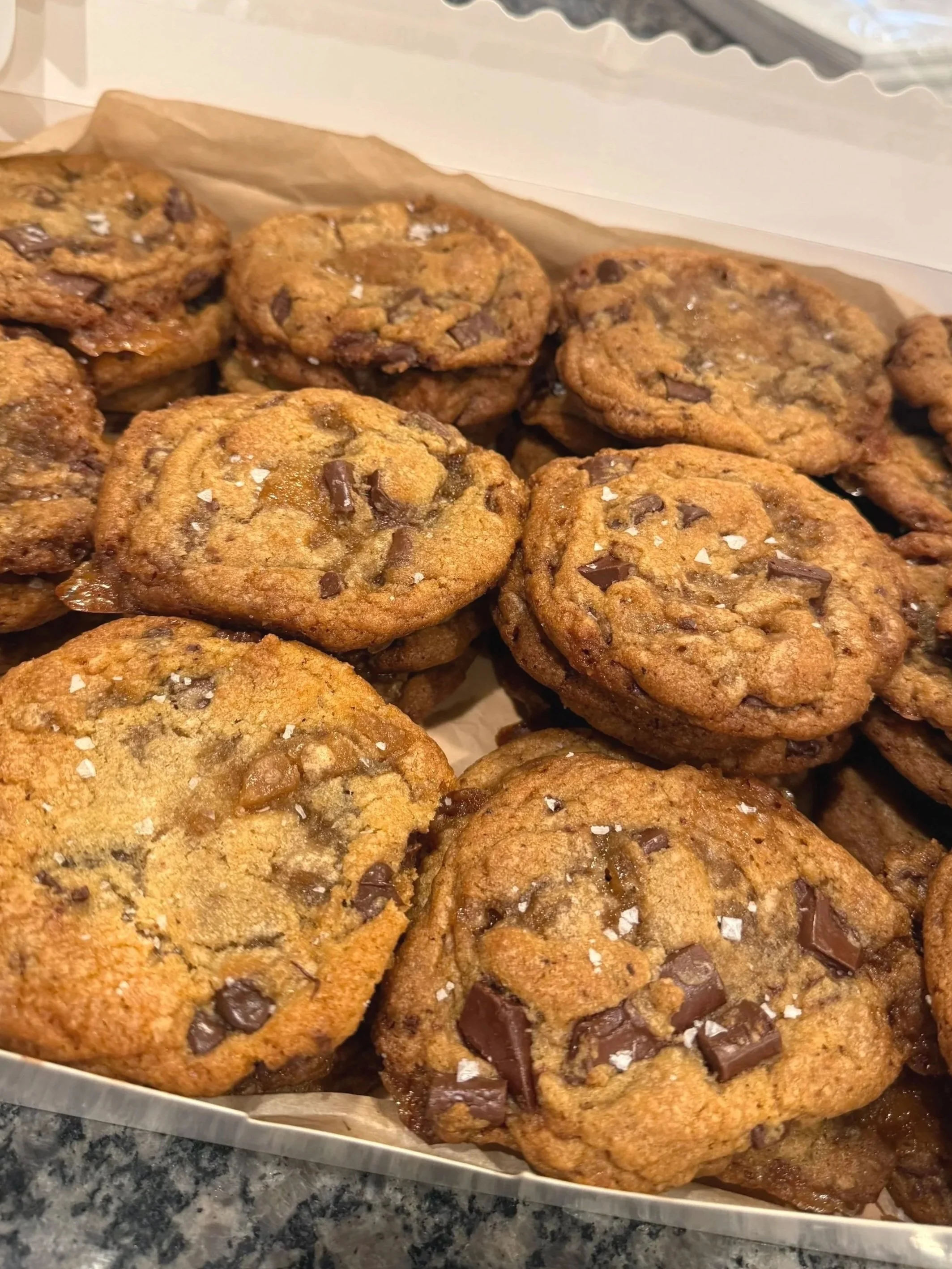 Close-up of a tray of freshly baked chocolate chip cookies sprinkled with sea salt on a parchment-lined tray.