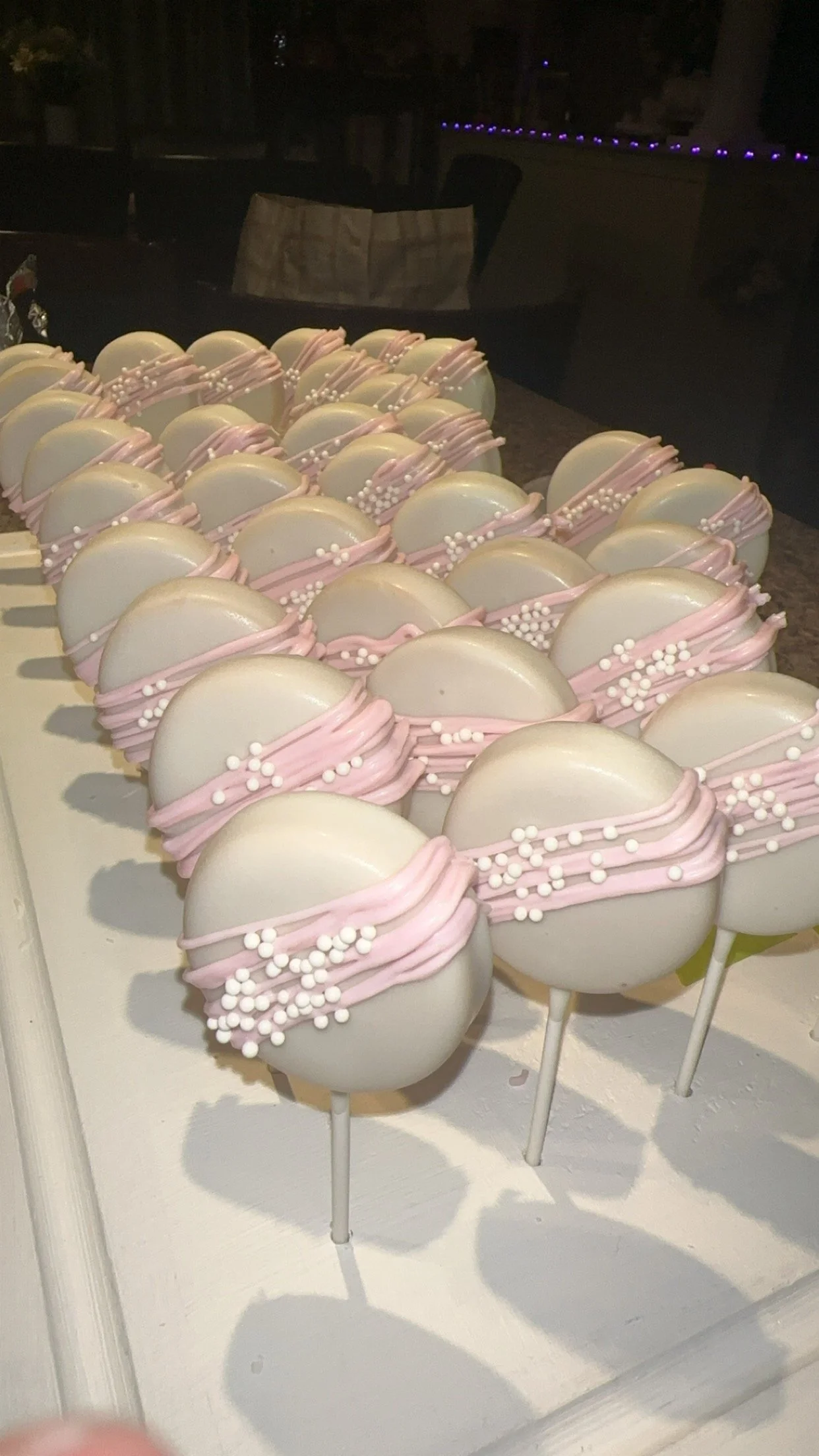 White cake pops decorated with pink icing and white sprinkles, arranged on a tray