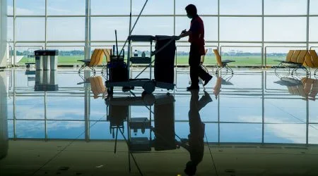 Janitor walking with cleaning cart in airport terminal with large windows and empty seats