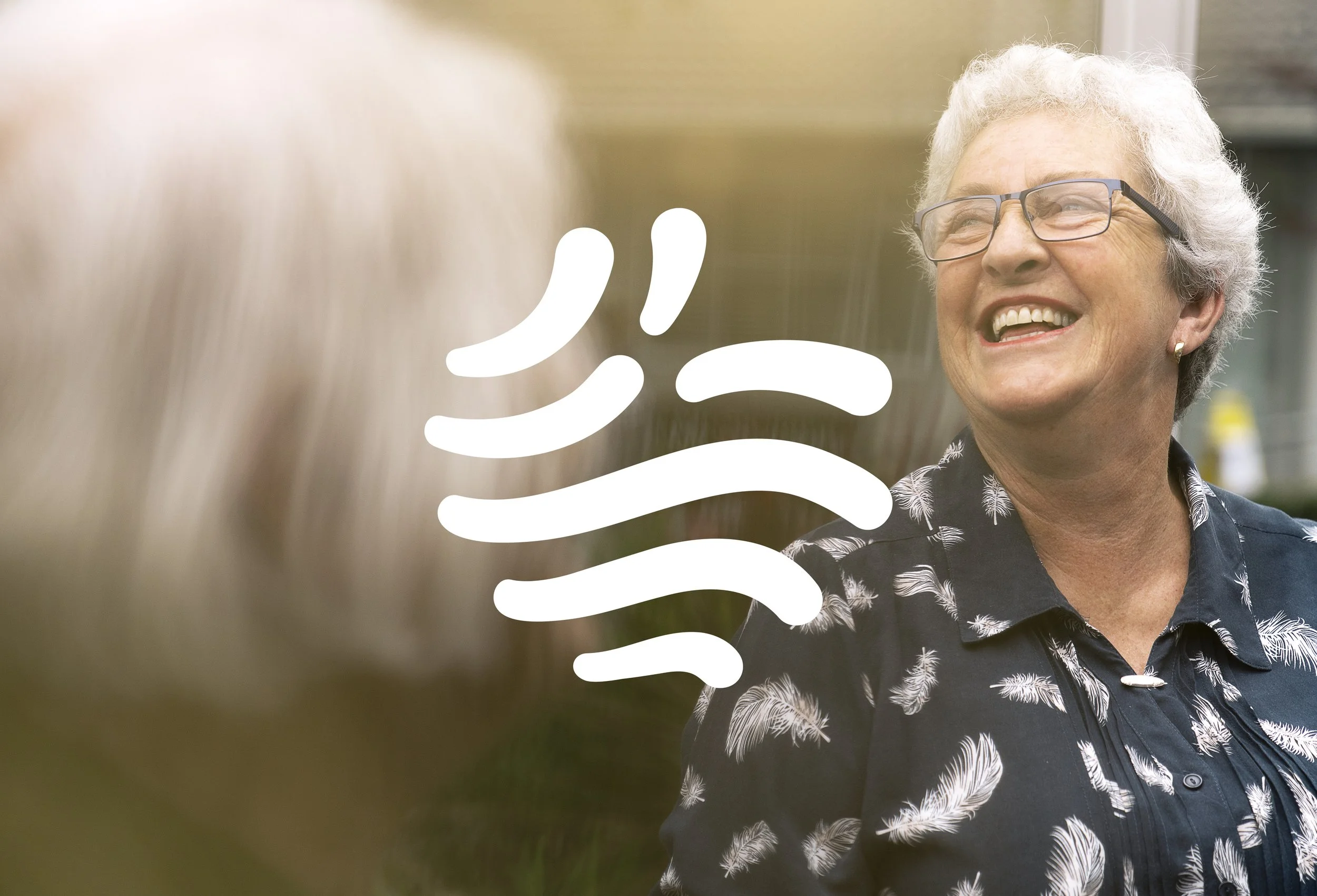 An elderly woman with short white hair and glasses smiling and looking to her right