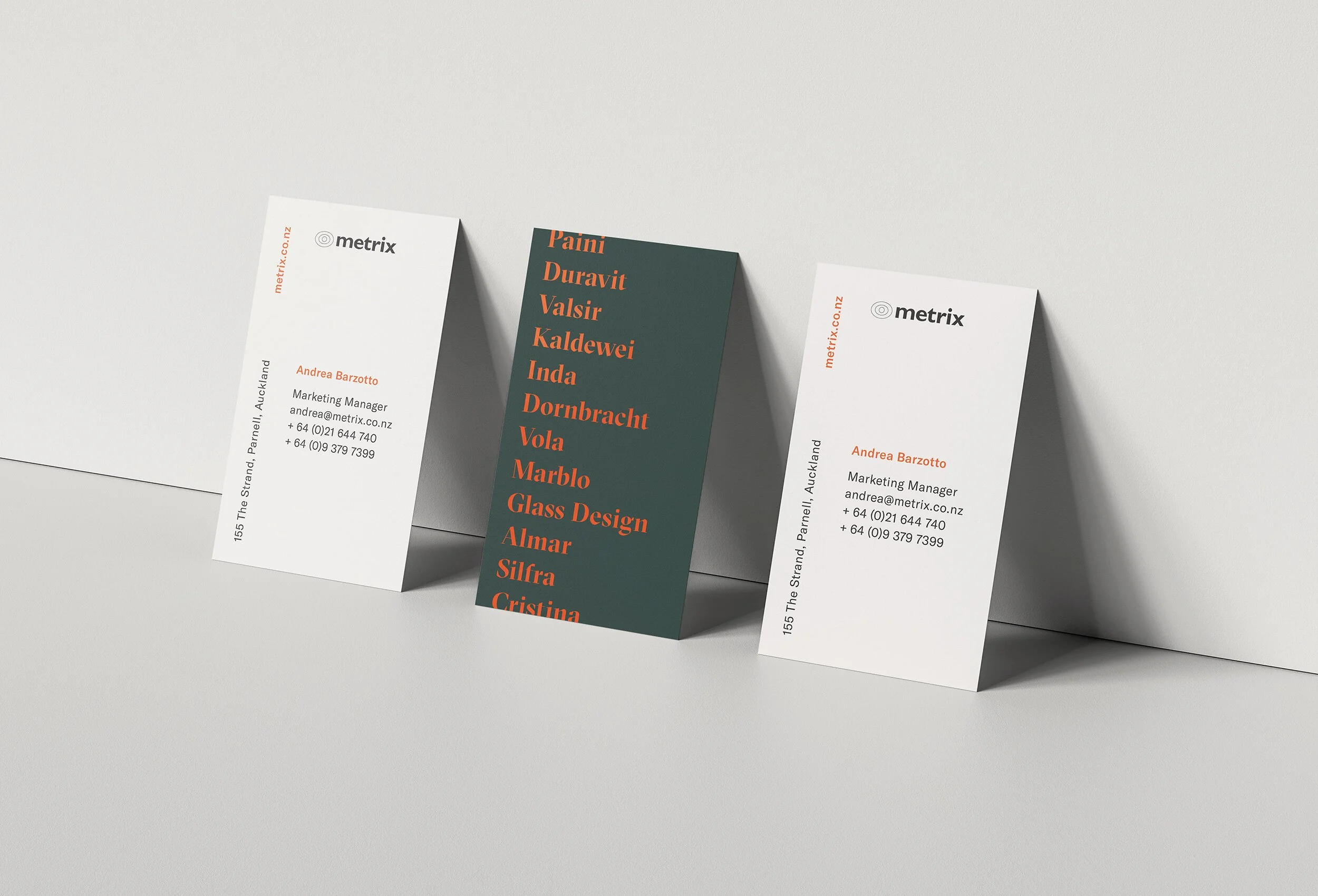 Three vertically arranged business cards on a surface, with the two outer cards displaying contact information and the middle card listing names.