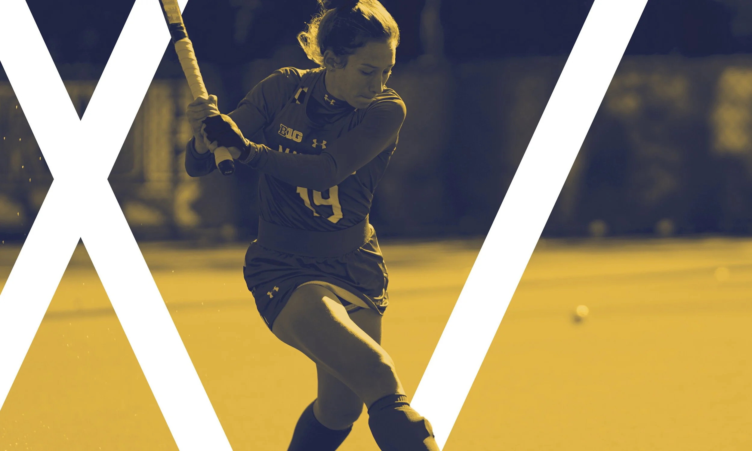 Female field hockey player in action, wearing a dark uniform with the words 'BIG' and 'U' visible, holding a hockey stick, on an outdoor field.