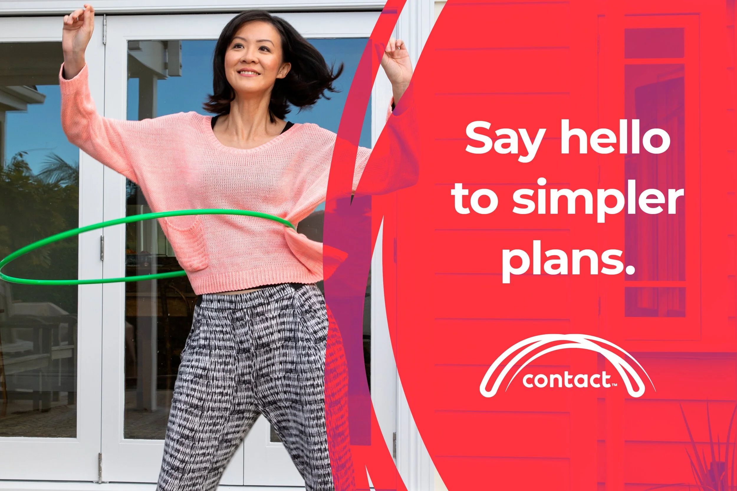 A woman in a pink sweater and patterned pants hula hoops outside in front of a glass door with a red and purple graphic overlay and the text 'Say hello to simpler plans.'