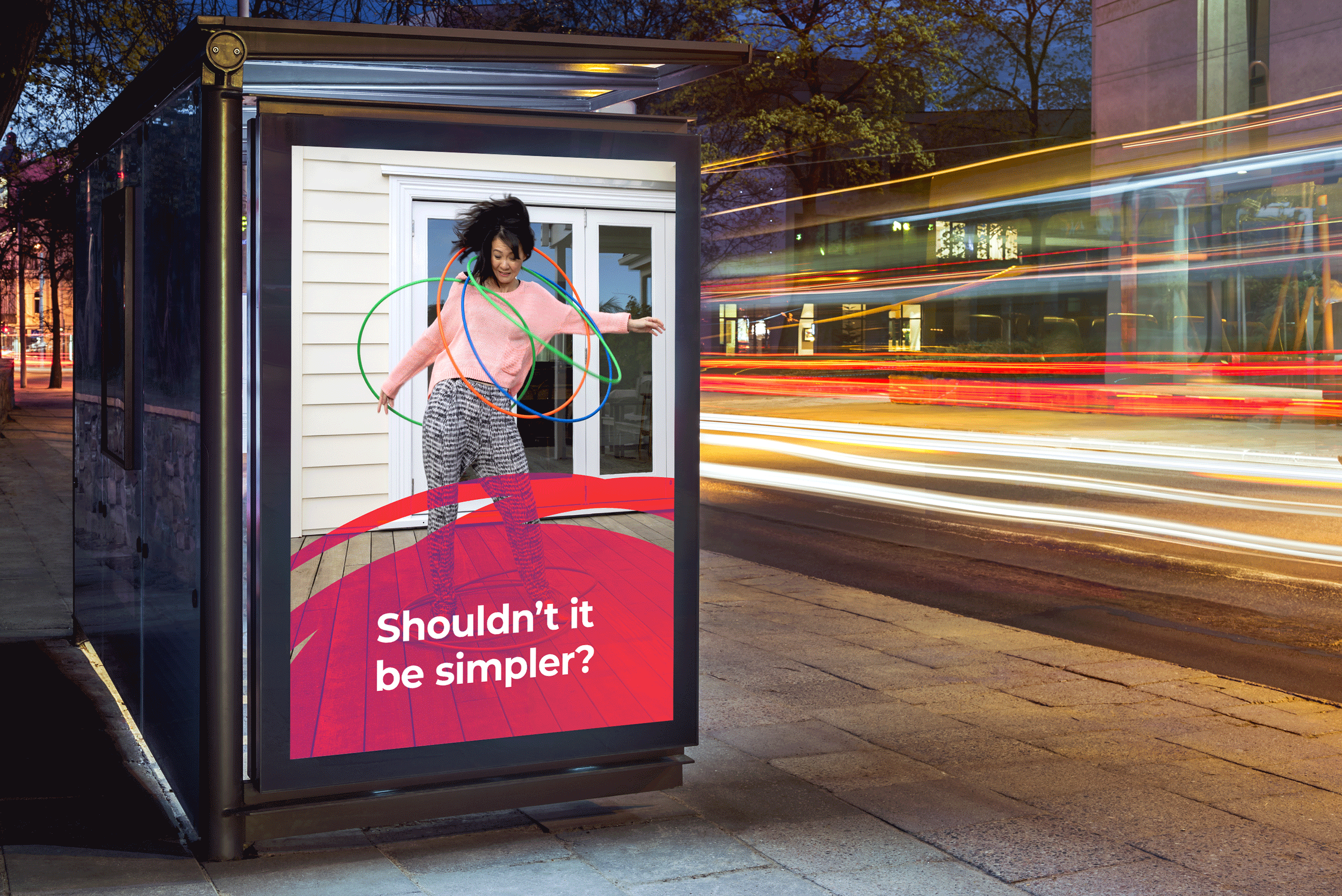 A woman jumping in a bus shelter with colorful glow-rings around her, light trails in the background, and a red sign with white text reading 'Shouldn't it be simpler?'