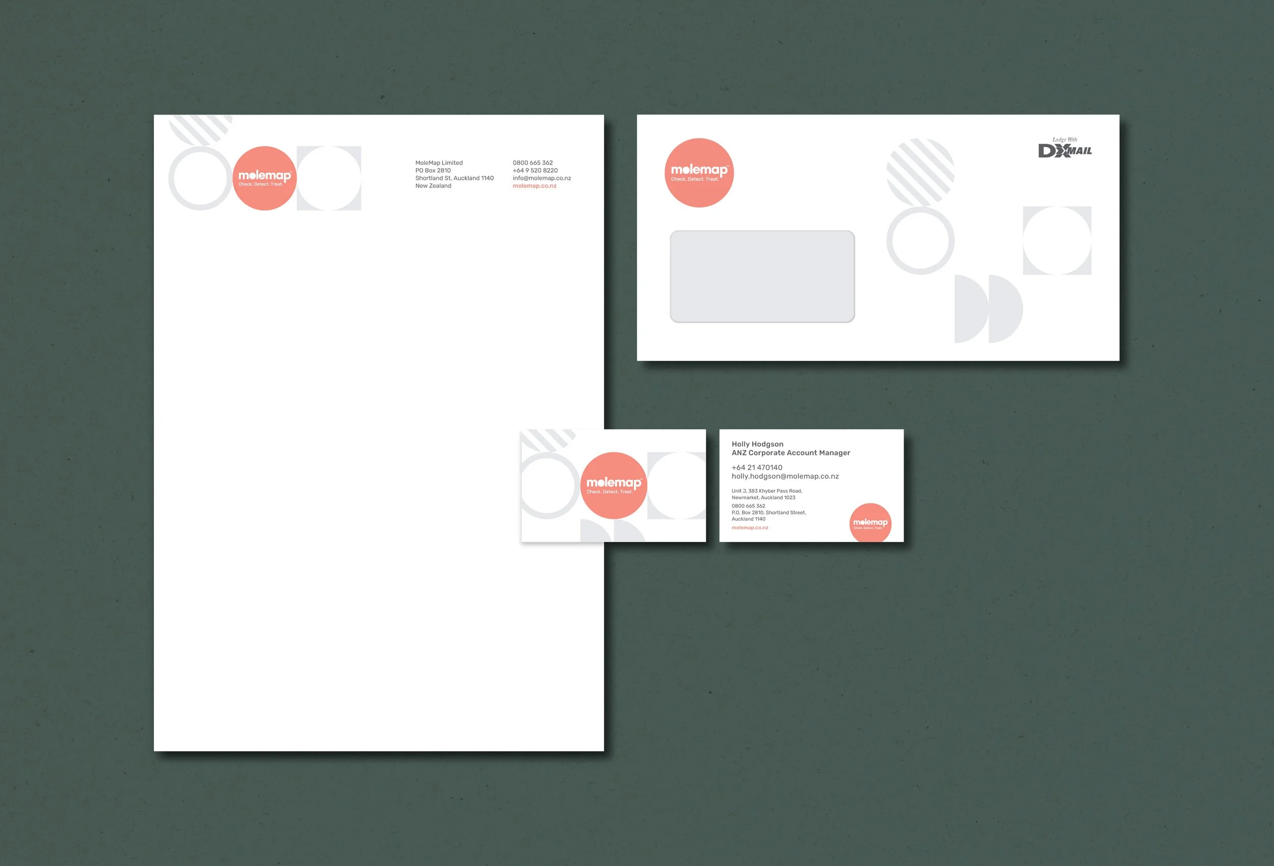 Set of business cards and envelope for Molemap, featuring a red logo, geometric patterns, and contact details, laid out on a green surface.
