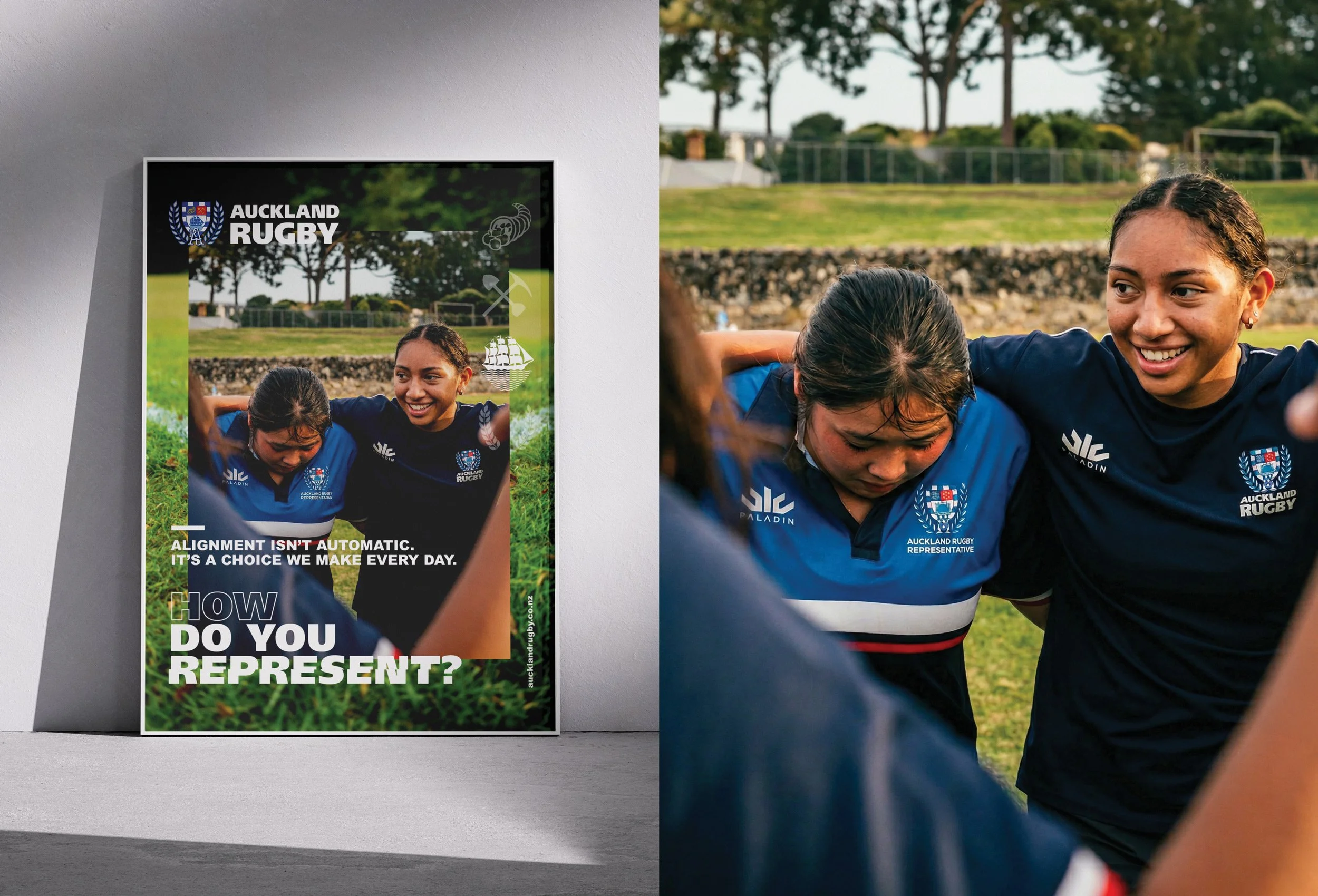 A poster of Auckland Rugby showing two female rugby players wearing blue jerseys with the Auckland Rugby logo, one with wet hair hugging the other, outdoors on a grassy field with trees in the background.