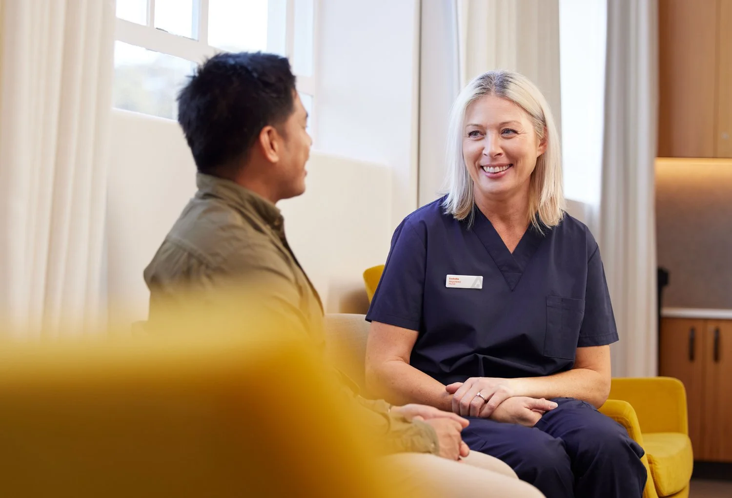 A female healthcare professional smiling and talking to a male patient in a medical facility.