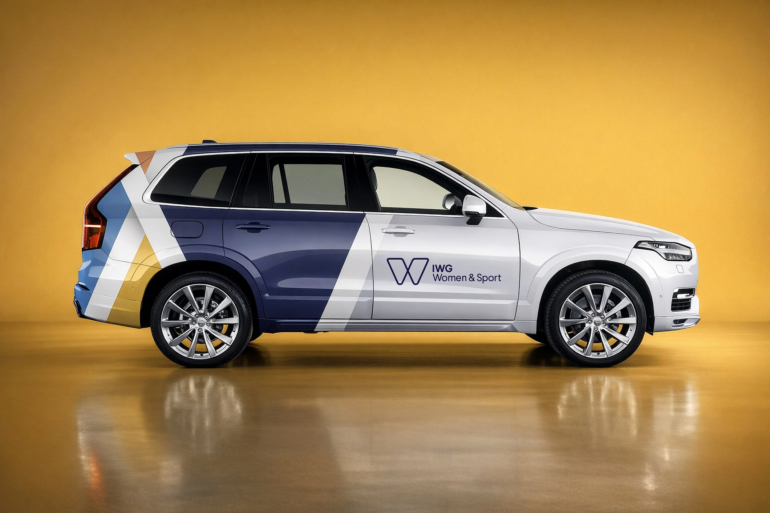 A white SUV with colorful geometric patterns and a logo for Women & Sport on the side, parked against a plain orange background.