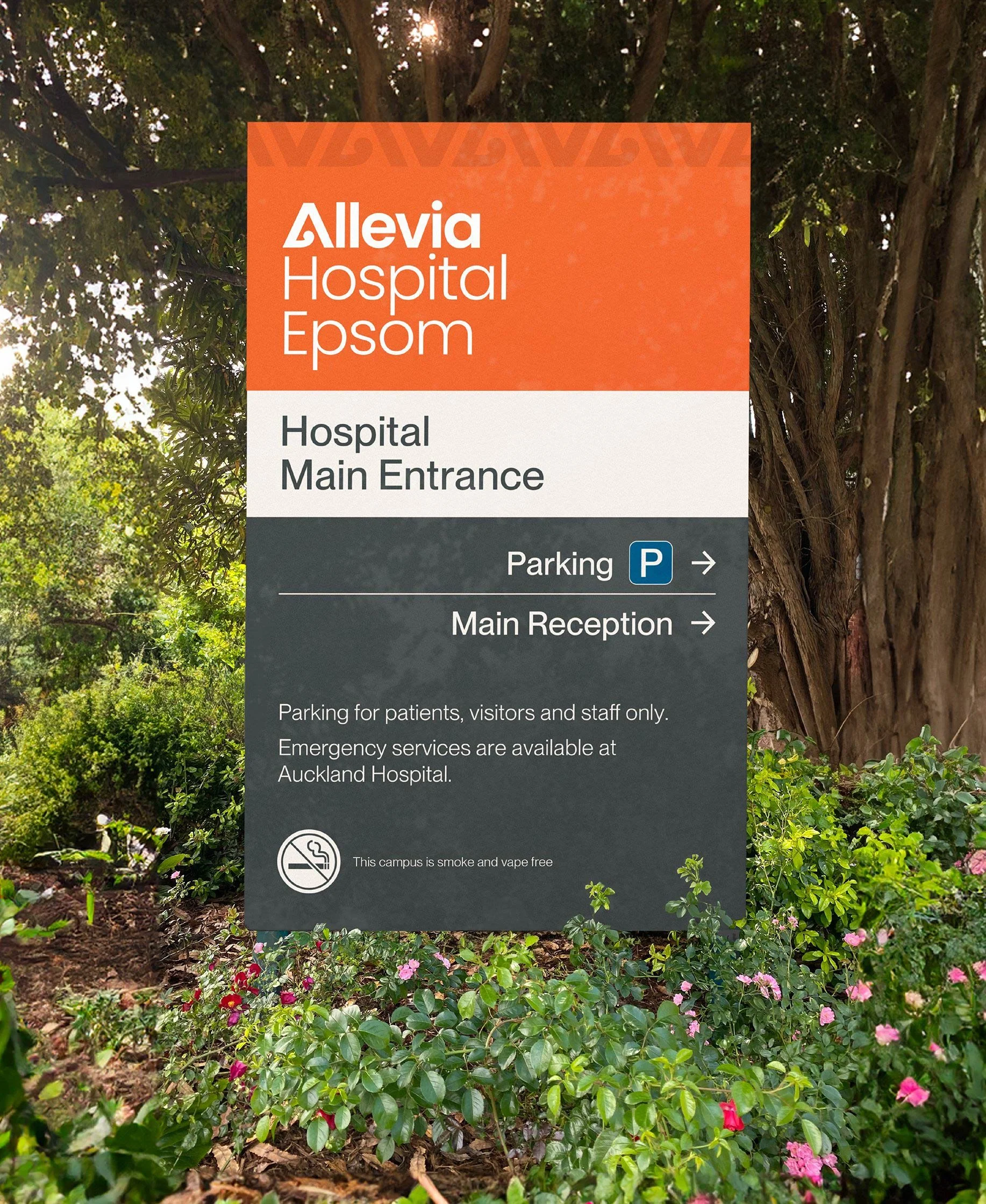 Sign at Auckland Hospital showing directions for main entrance and parking, with greenery and trees in the background.