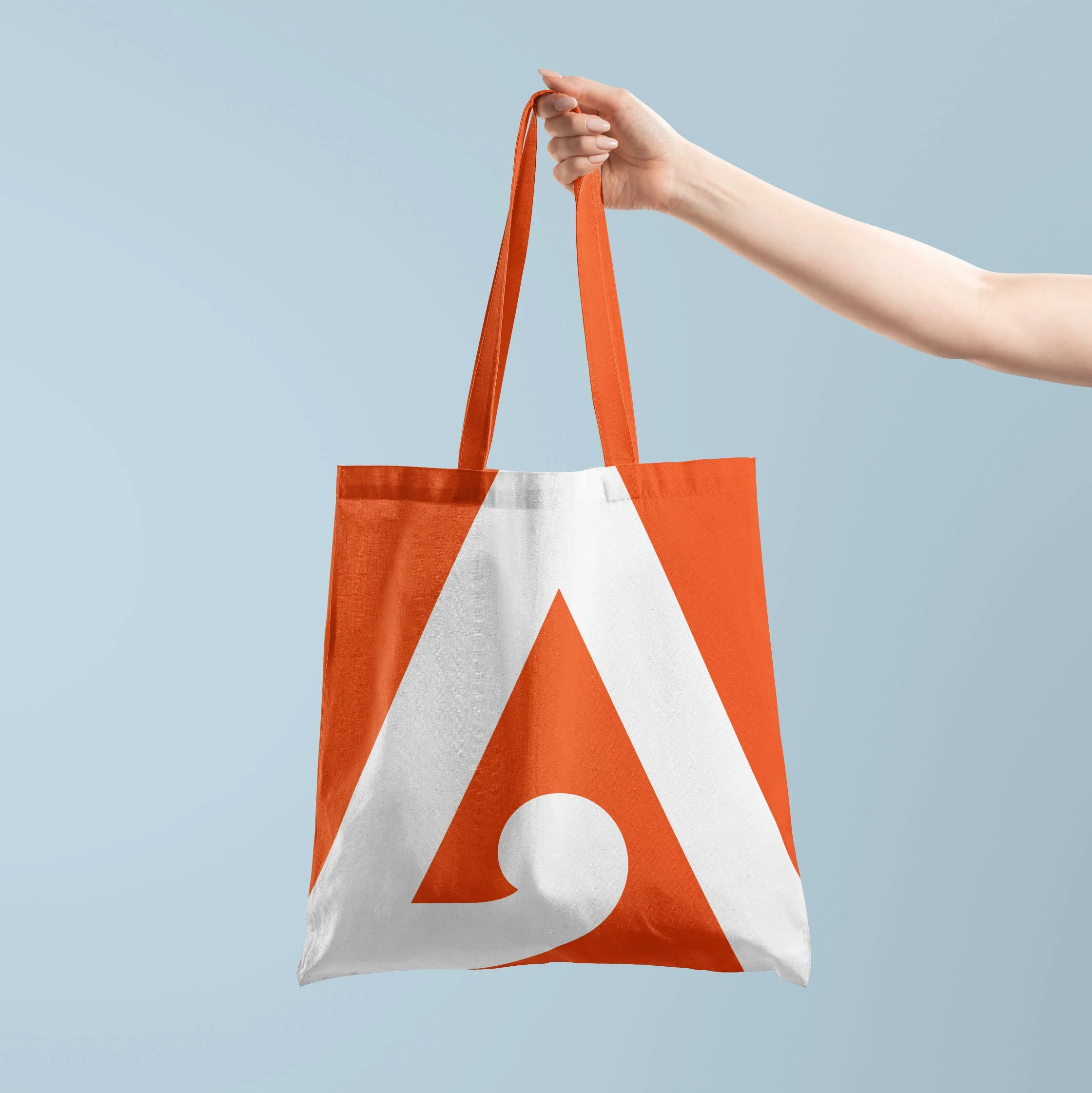 A person holding a reusable shopping bag with orange handles and a white and orange design against a light blue background.