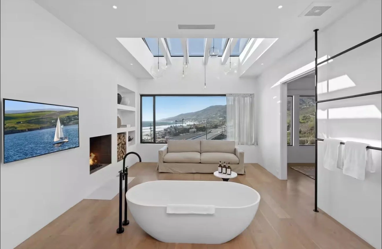 Modern living room with a bathtub in the center and a view of the ocean and mountains through large windows