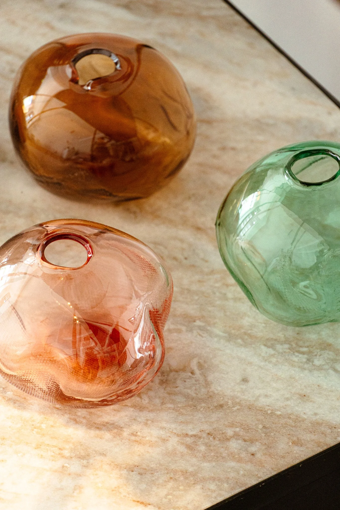 Bunte bauchige Glasvasen in Orange, Grün und Transparent auf einer hellen Holzfläche.