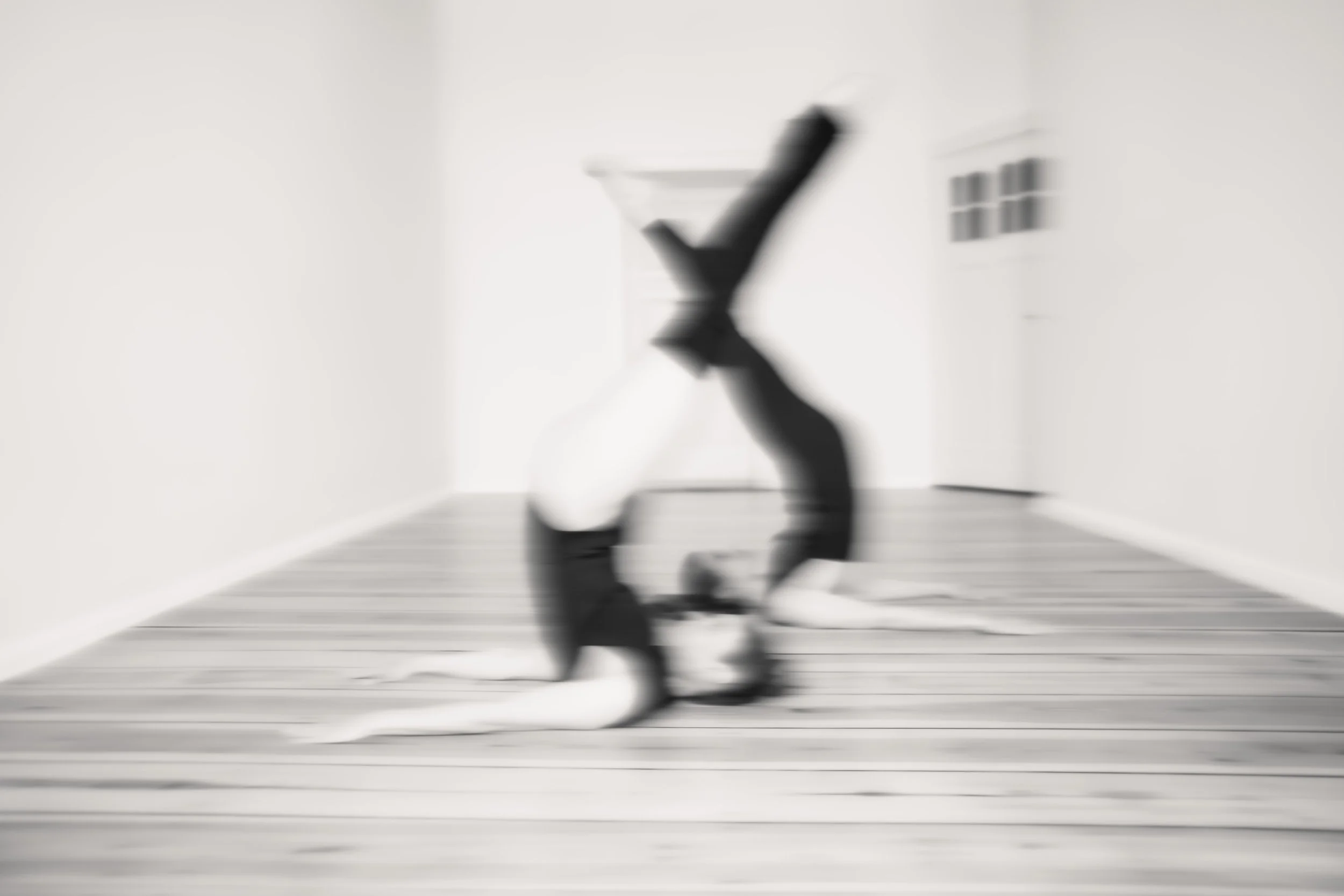 Bewusst unscharfes Schwarz-Weiß-Foto von Mimi und Lucie in einer Pilates Pose "Jack Knife" auf dem Holzboden im leeren Raum.