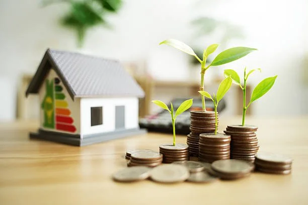 Miniatuur huis naast rij van coin-stapels met groene plant die groeit