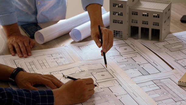 Architecten die bouwtekeningen bestuderen met een miniatuurmodel op tafel.