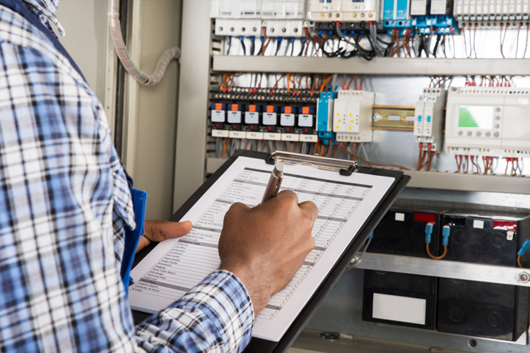 Technicus die een controlelijst invult in een elektrische kast met schakelaars en draden.
