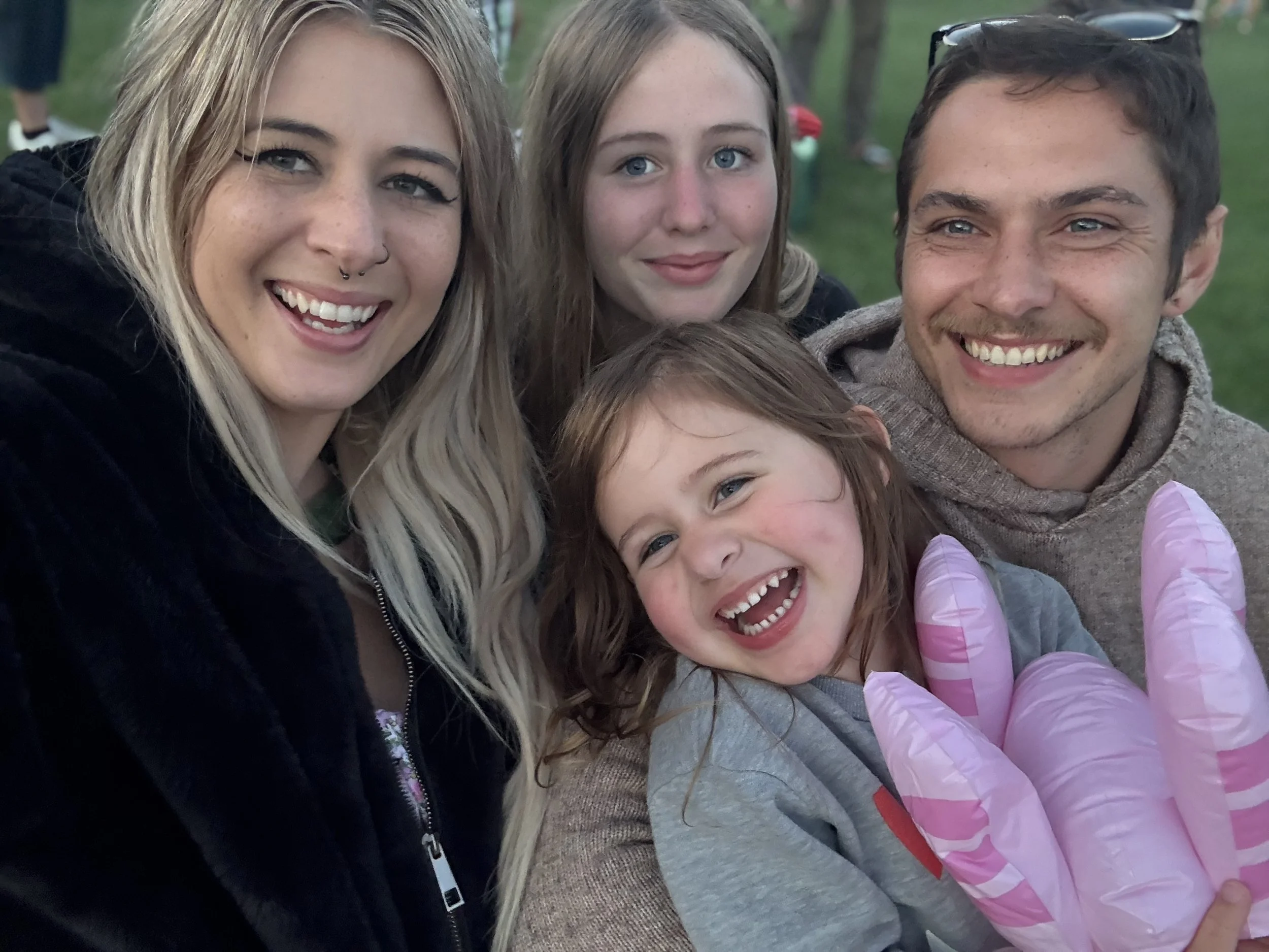 A group of five smiling people, including two young girls, an older girl, and two young adults, posing outdoors.