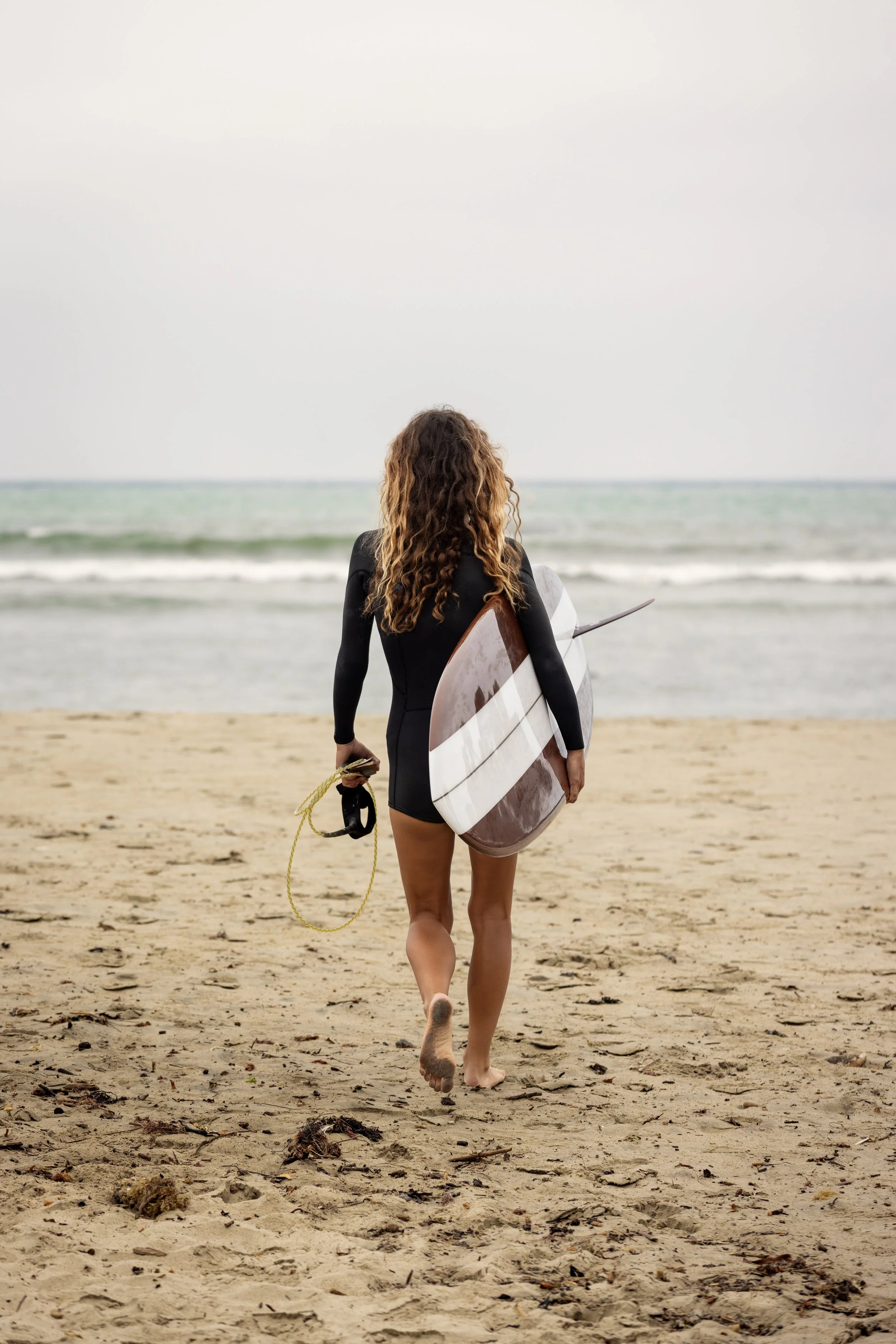Louise walking toward water on beach with surfboard.JPG