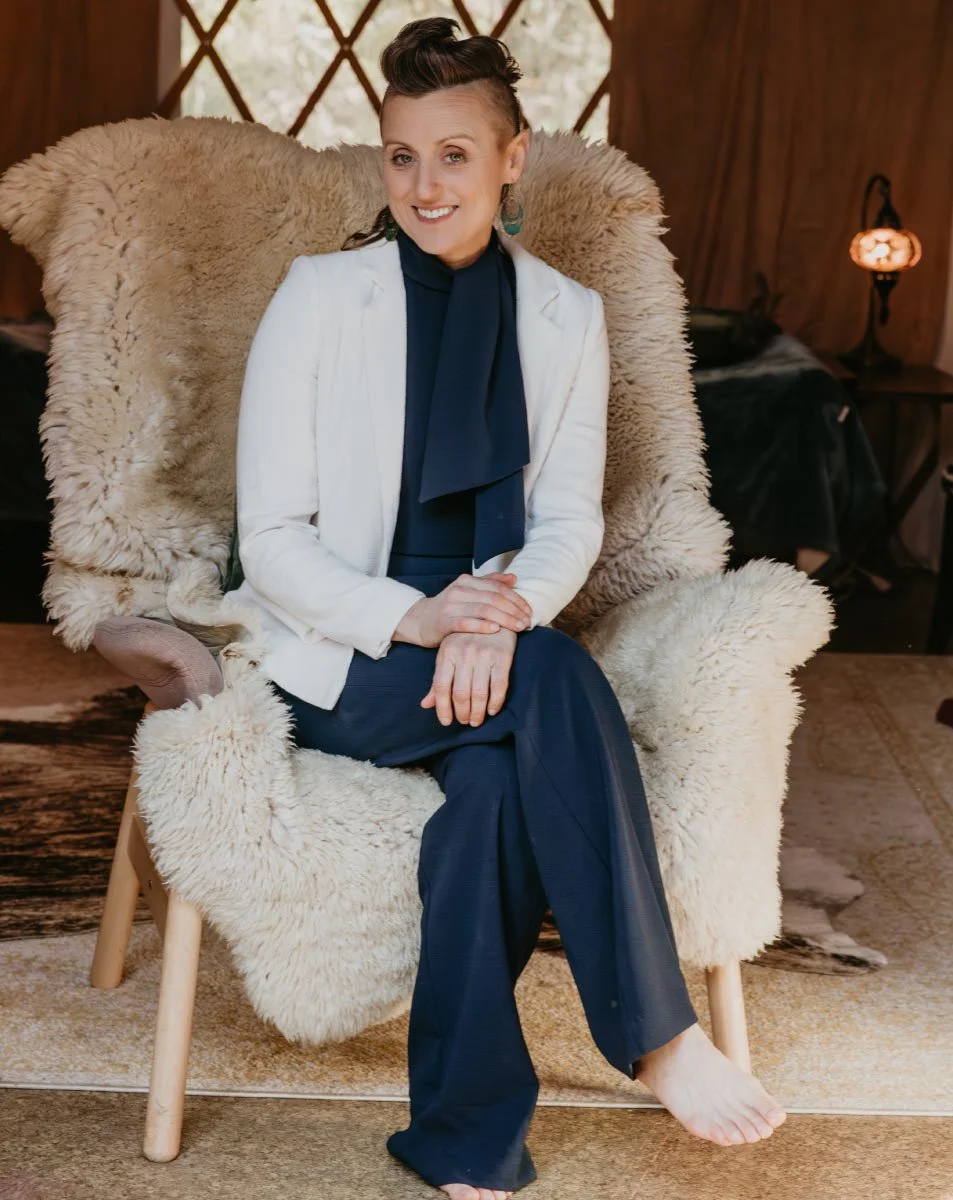 Woman sitting on a plush armchair with sheepskin covering, smiling, in a cozy wooden interior.