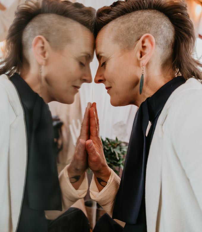 Non binary human looking sad and leaning head on mirror with the reflection on the left side