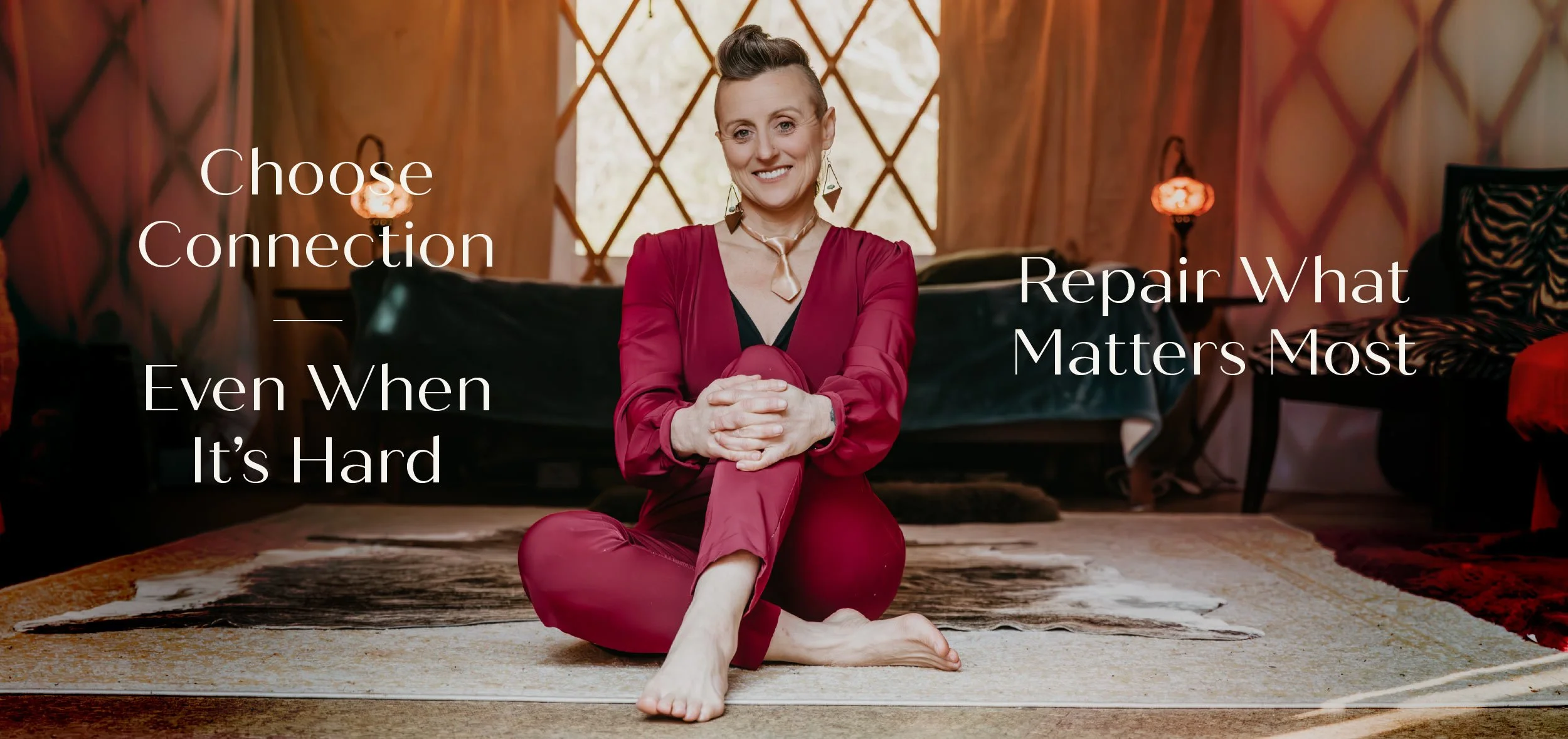 A woman sitting cross-legged on a rug in a cozy, warmly lit room with wooden walls and large windows, smiling at the camera. Overlaid text reads: 'Choose Connection Even When It’s Hard — Repair What Matters Most.'