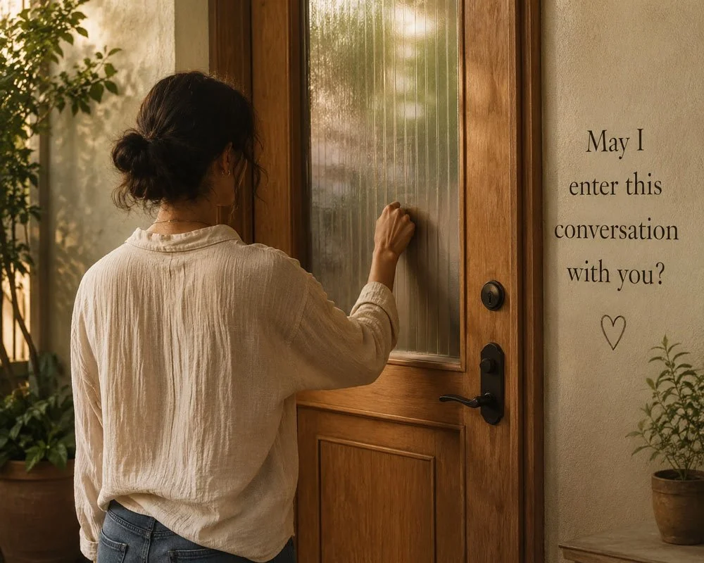 A woman with dark hair in a bun, wearing a beige blouse, is knocking on a wooden door with a frosted glass panel, next to a wall with a sign that says 'May I enter this conversation with you?' with a small heart symbol, and a potted plant beside it.