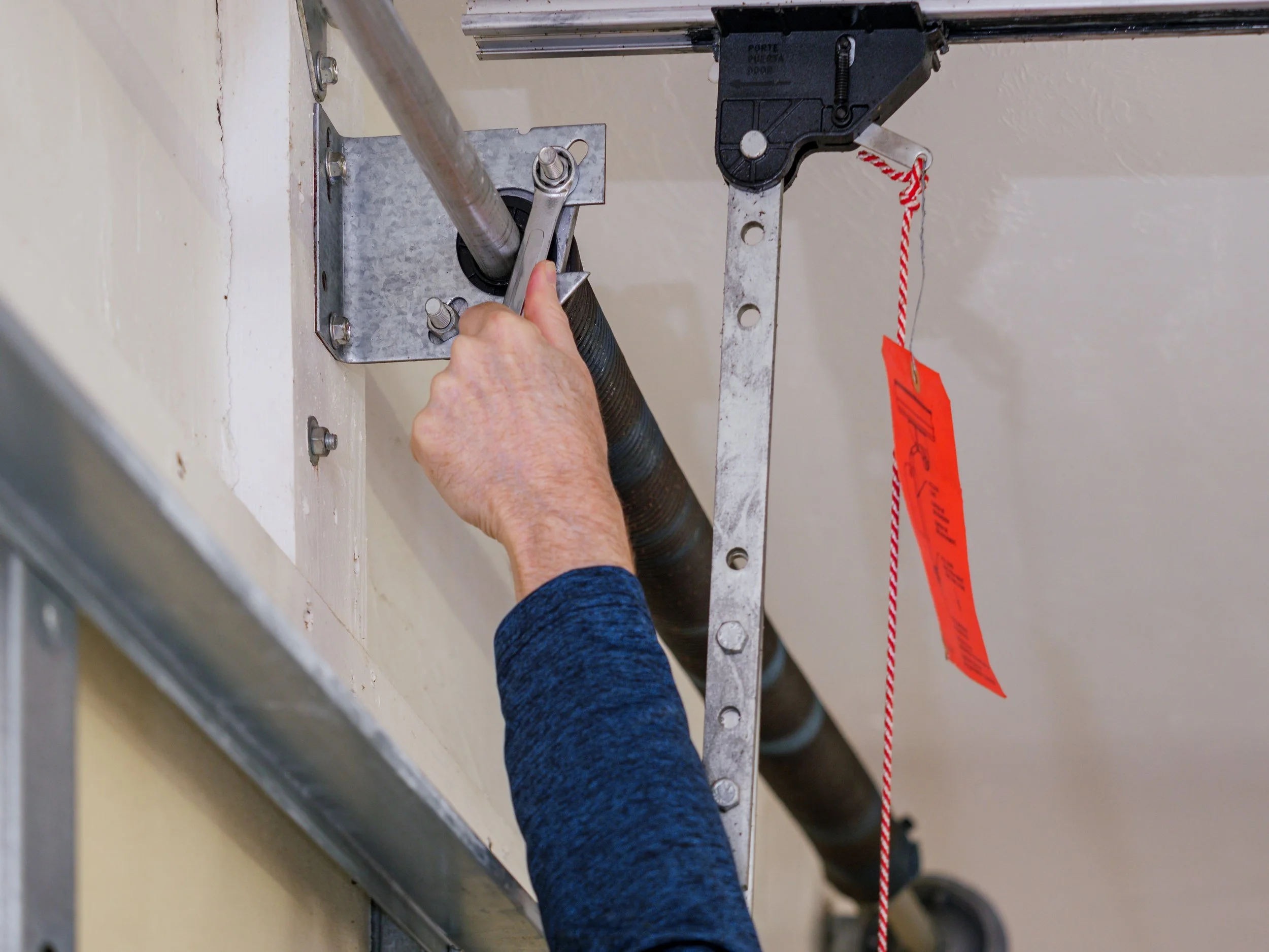 A person using a wrench to tighten or loosen a bolt on a metal mounting bracket attached to a wall; part of an industrial or maintenance setup.