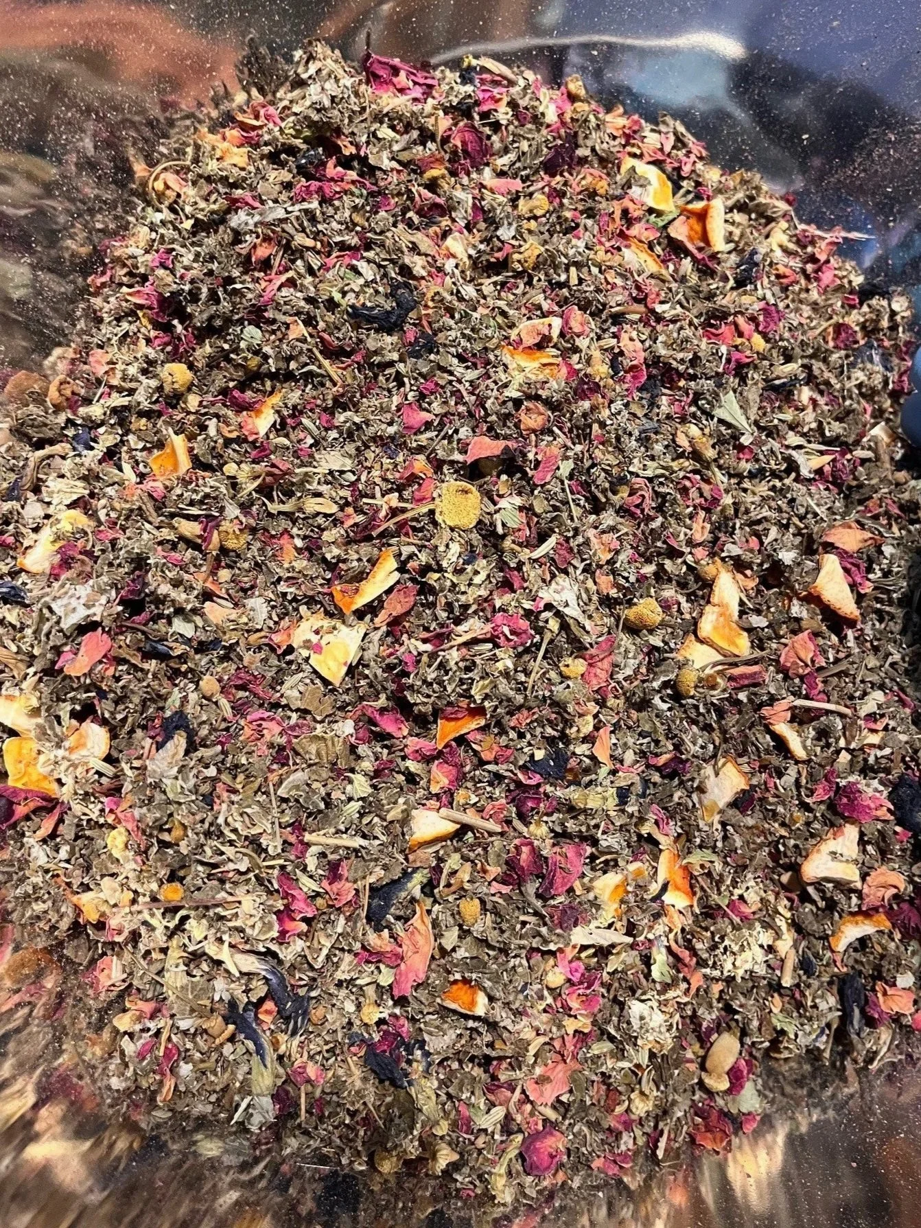 A mixture of dried herbs and flower petals in a metal container.