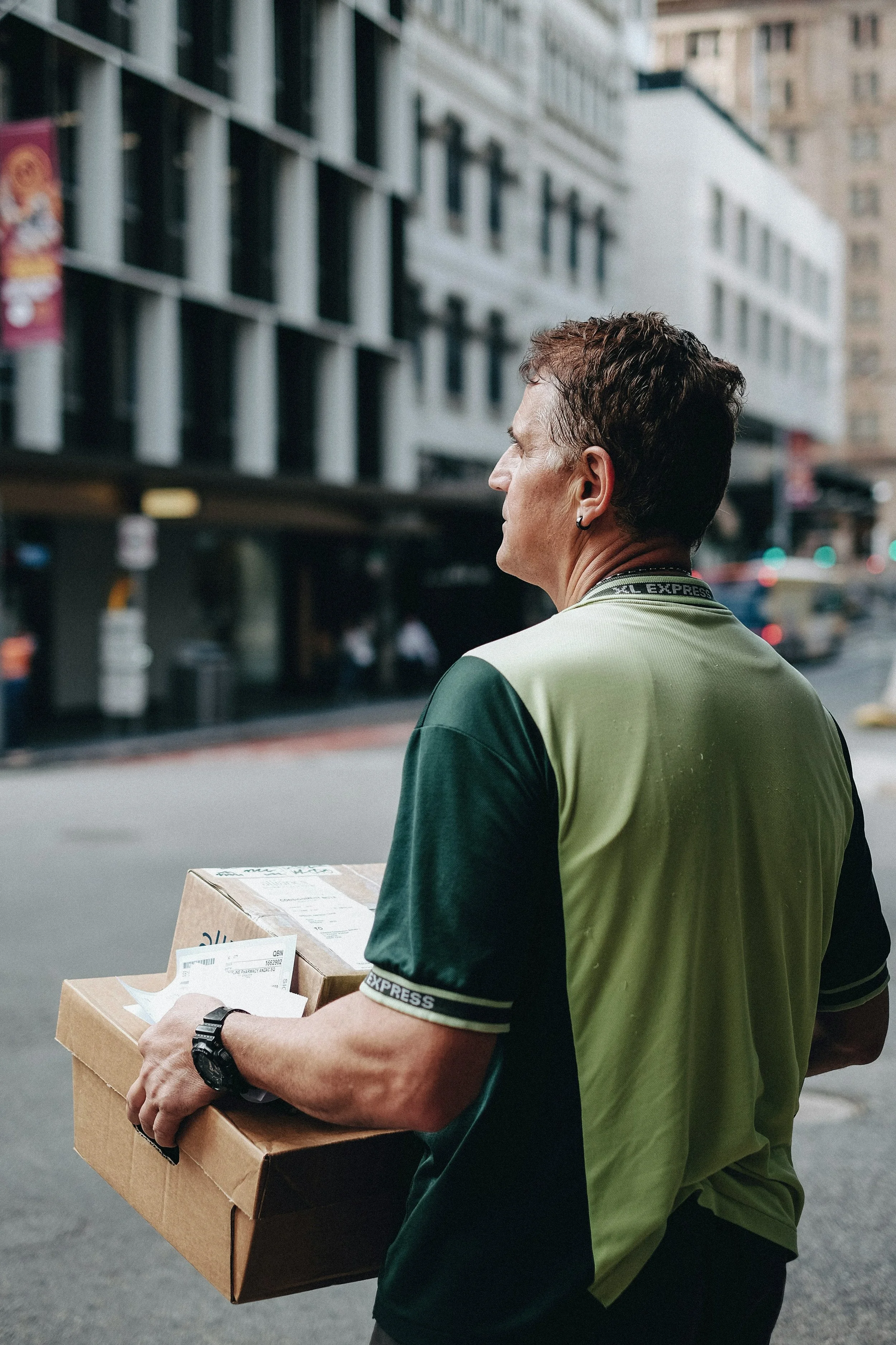 A man carrying two cardboard boxes with packages in an urban street.
