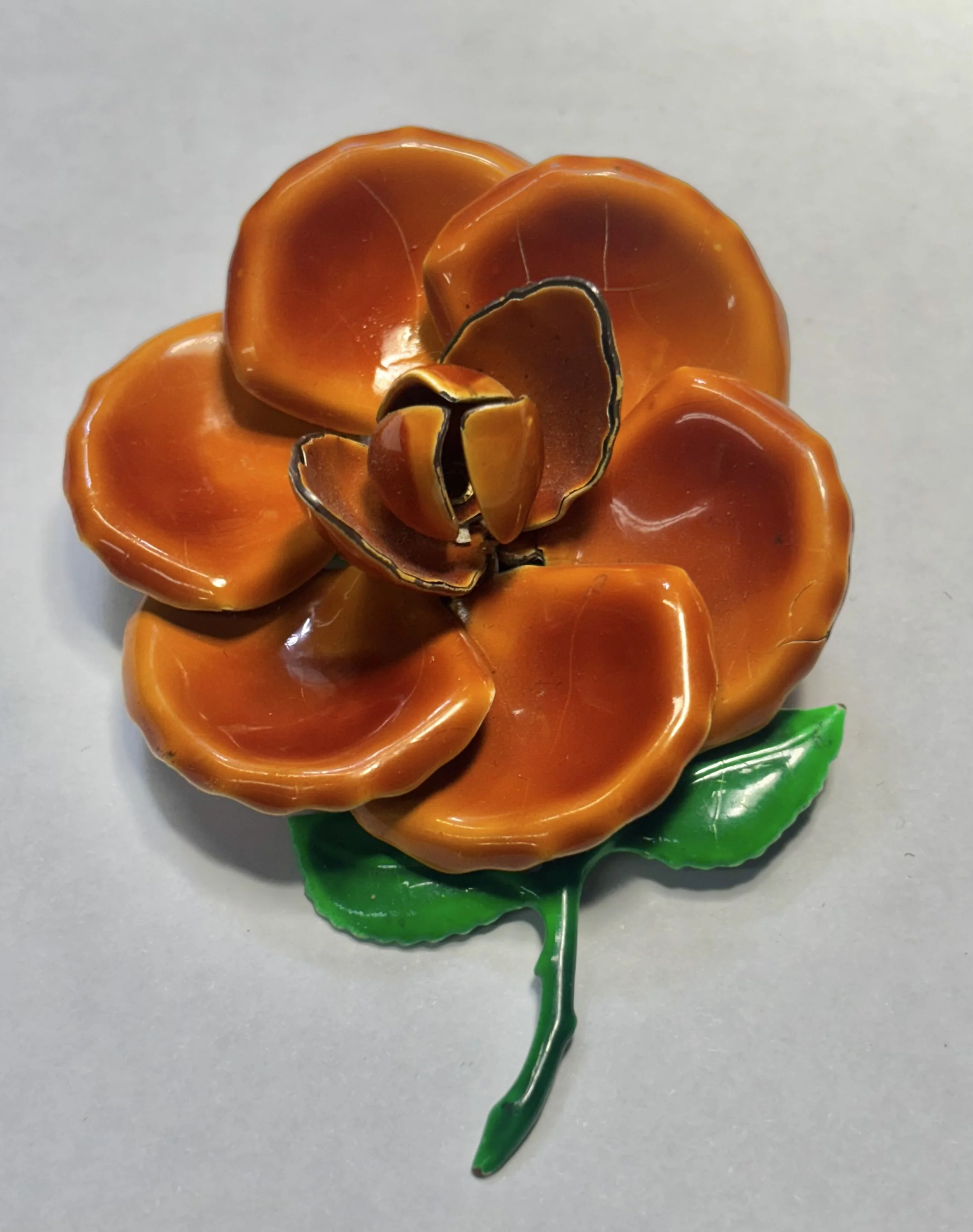 A decorative plastic flower with orange petals, green leaves, and a green stem.