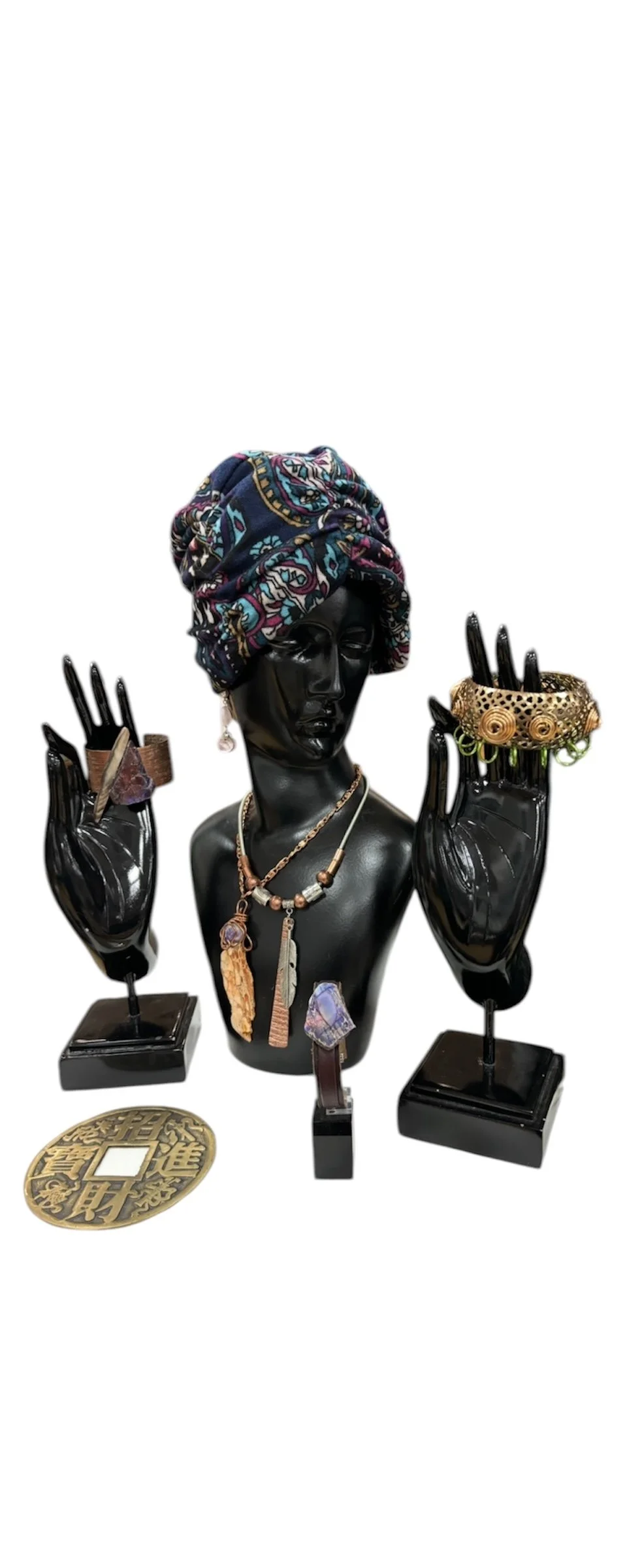 Jewelry display featuring a black mannequin bust adorned with necklaces, rings, bracelets, and a colorful headscarf, set against a white background.