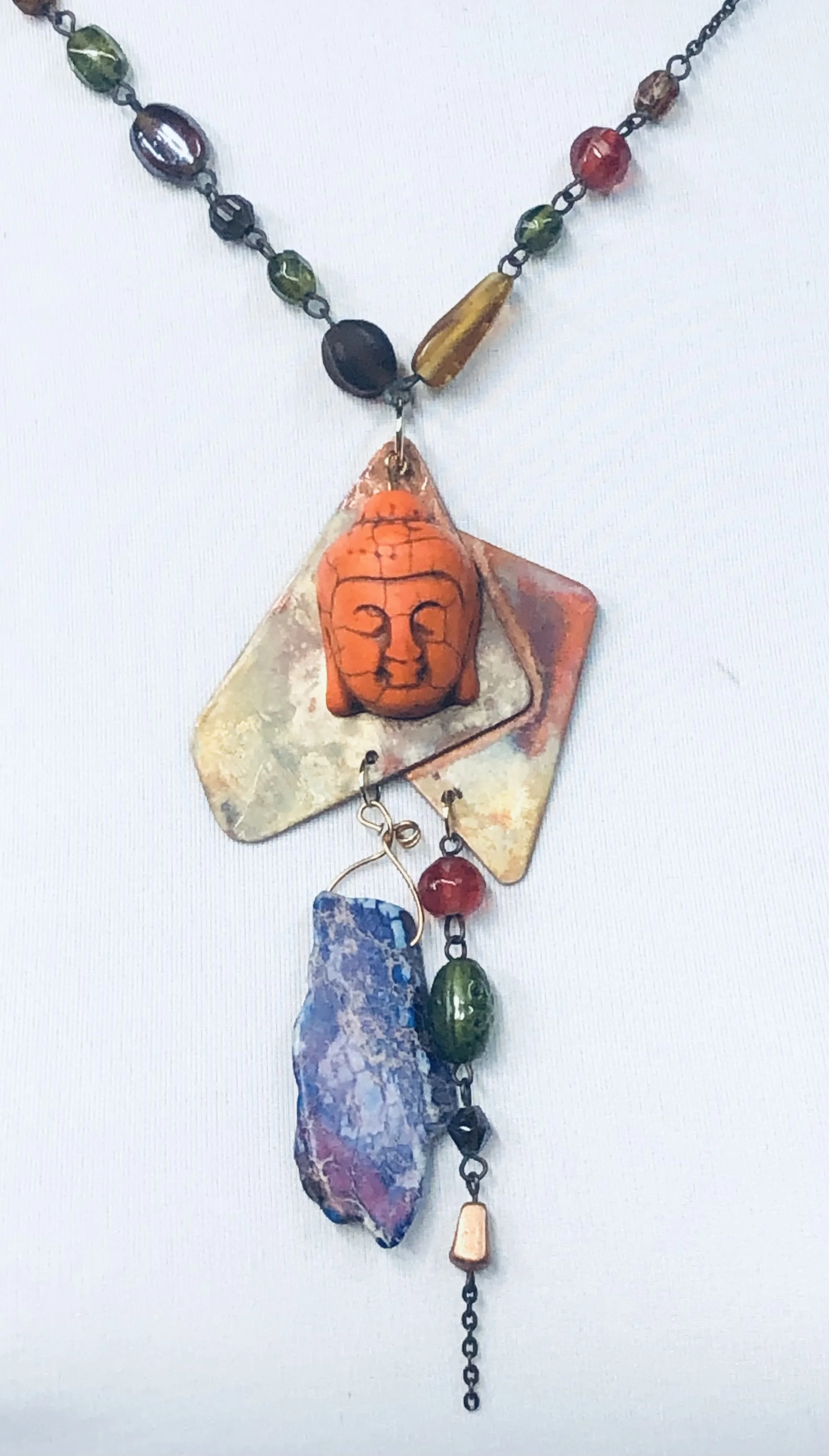Colorful beaded necklace with an orange face pendant, irregularly shaped stones, and small beads on a chain.
