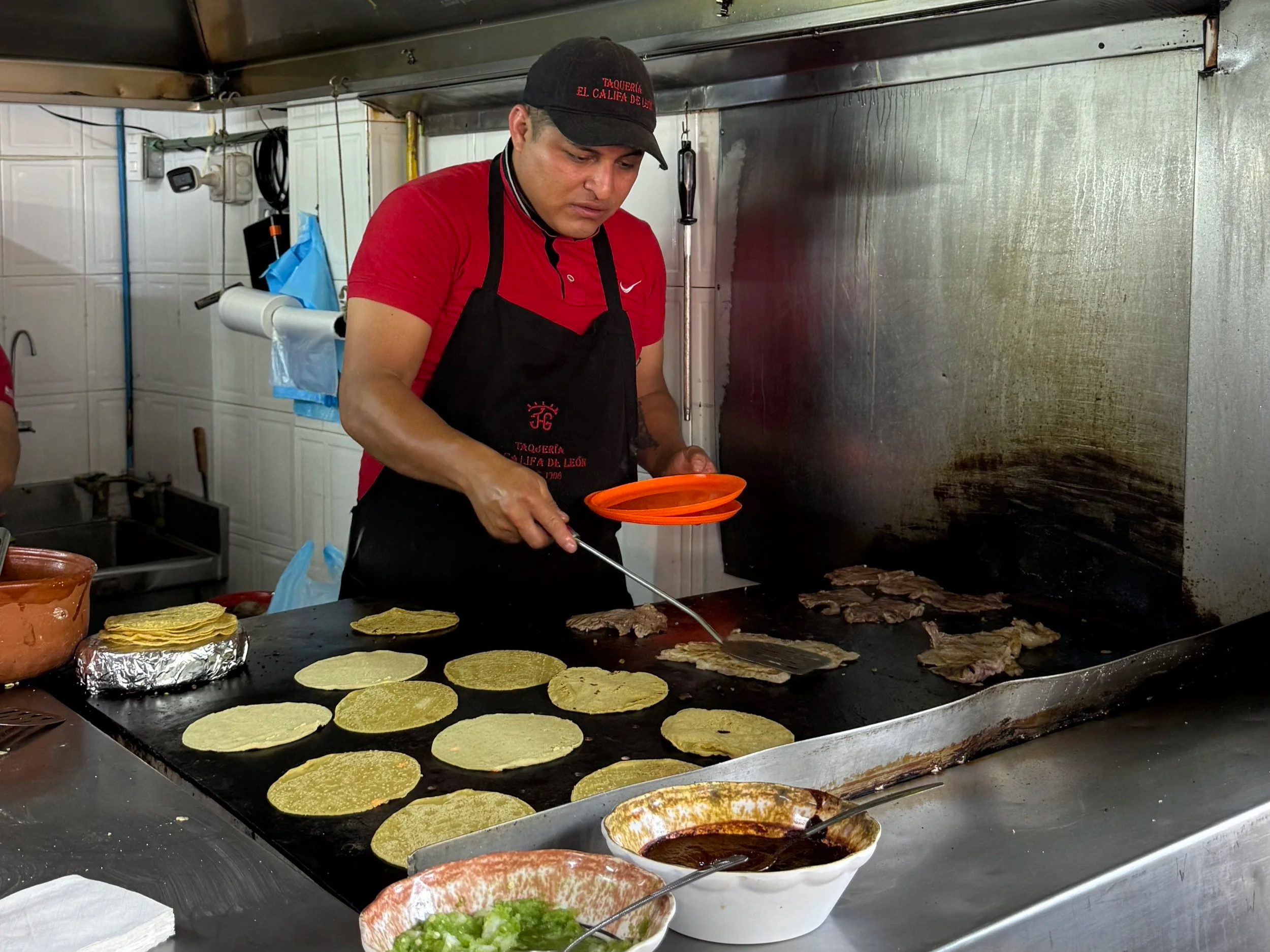 Cook grilling fresh tortillas and meat at El Califa de León taco stand in Mexico City
