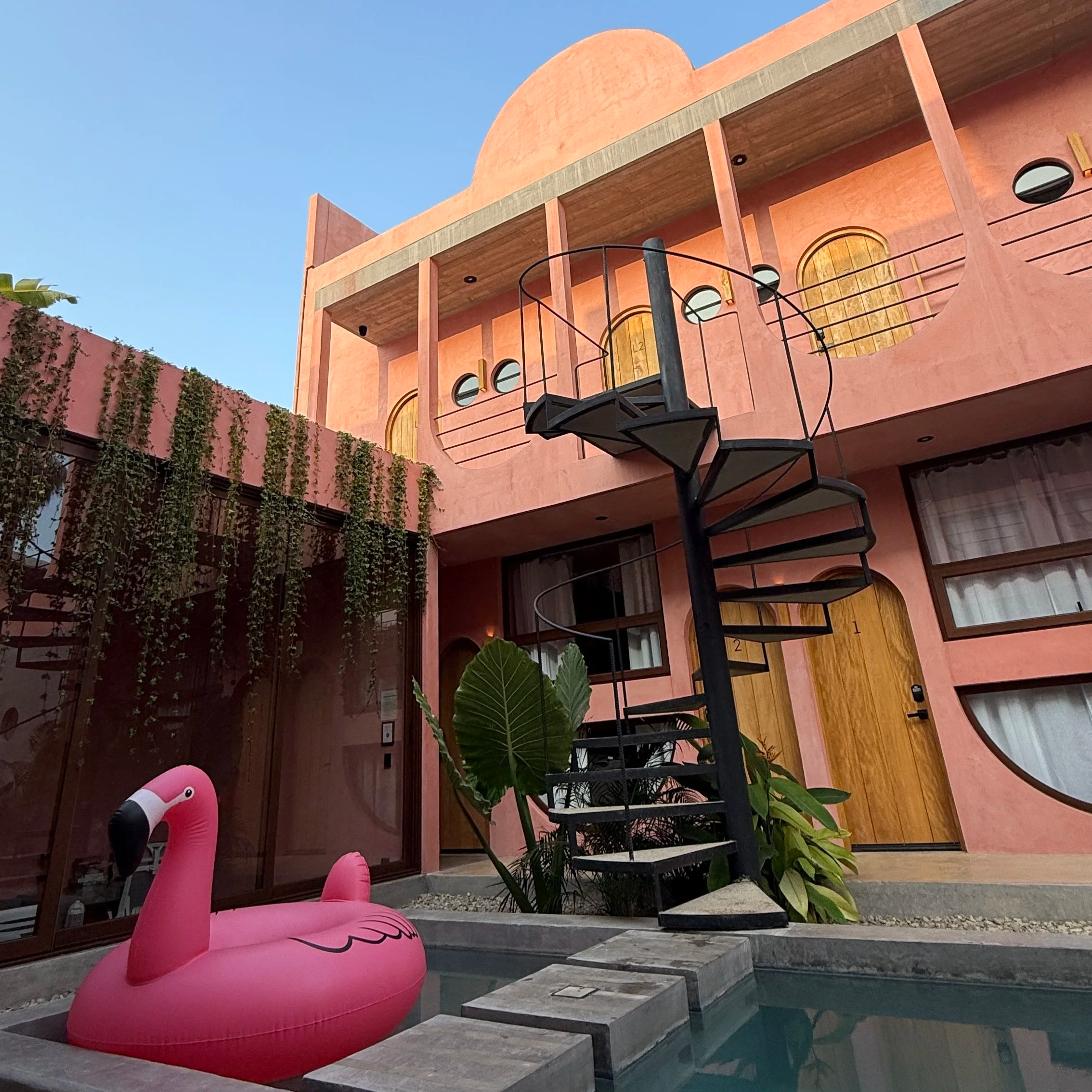 Interior of Amplitude Co-Living House with it's pink exterior including a spiral staircase and pink inflatable flamingo in the pool