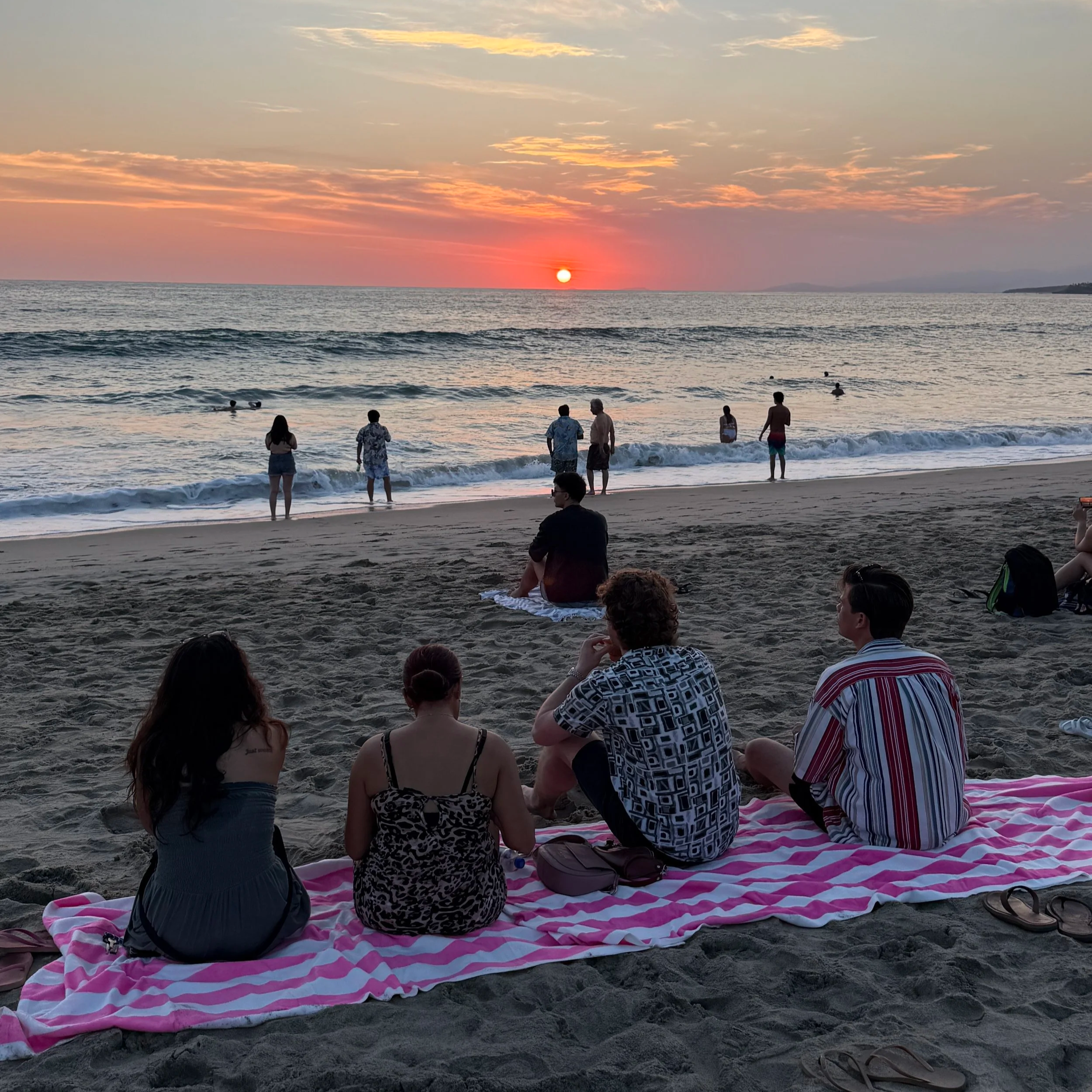 Friends sitting together on the beach watching sunset in Puerto Escondido, Mexico