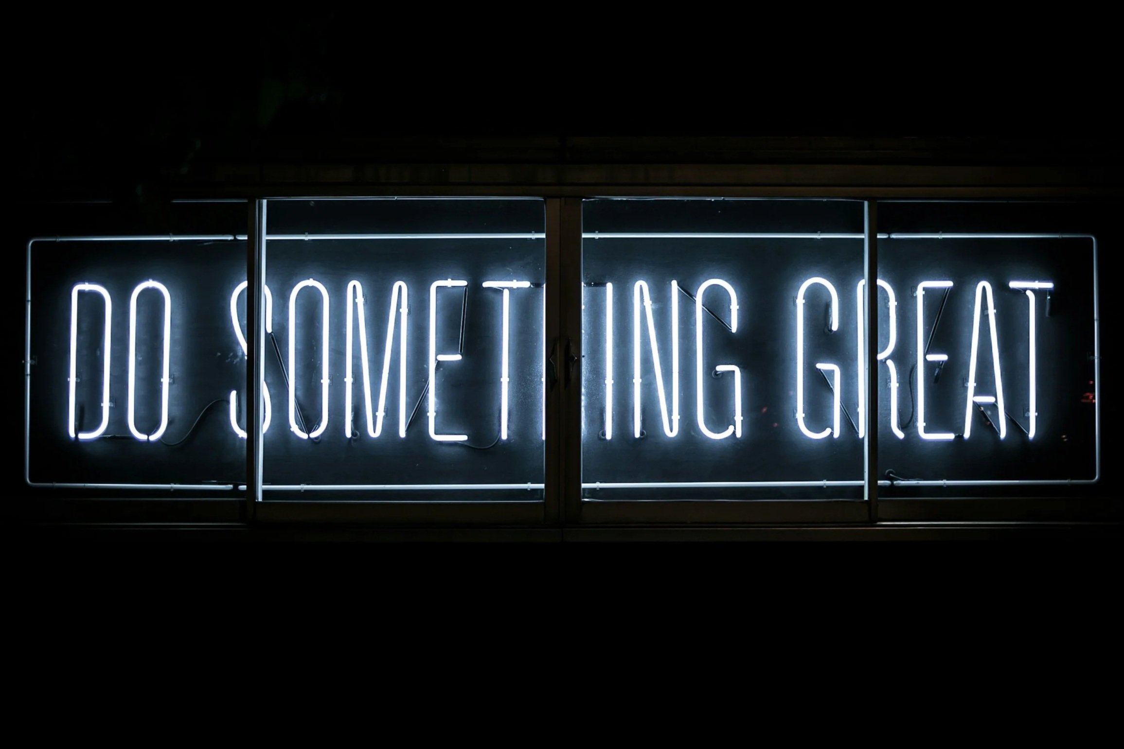 Neon sign displaying the phrase 'DO SOMETHING GREAT' in white letters against a dark background.