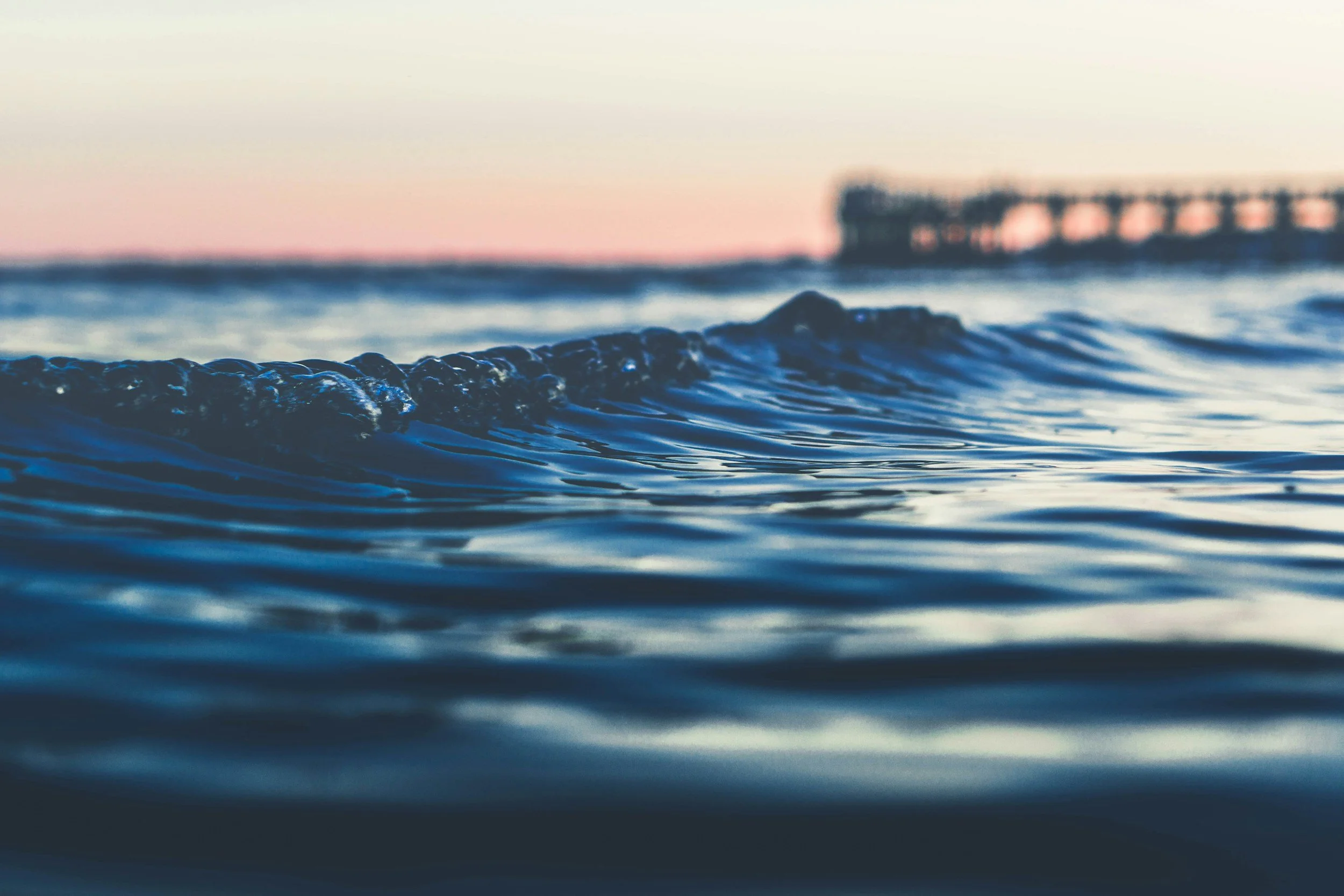 Close-up of ocean waves near a pier with a scenic sunset in the background.