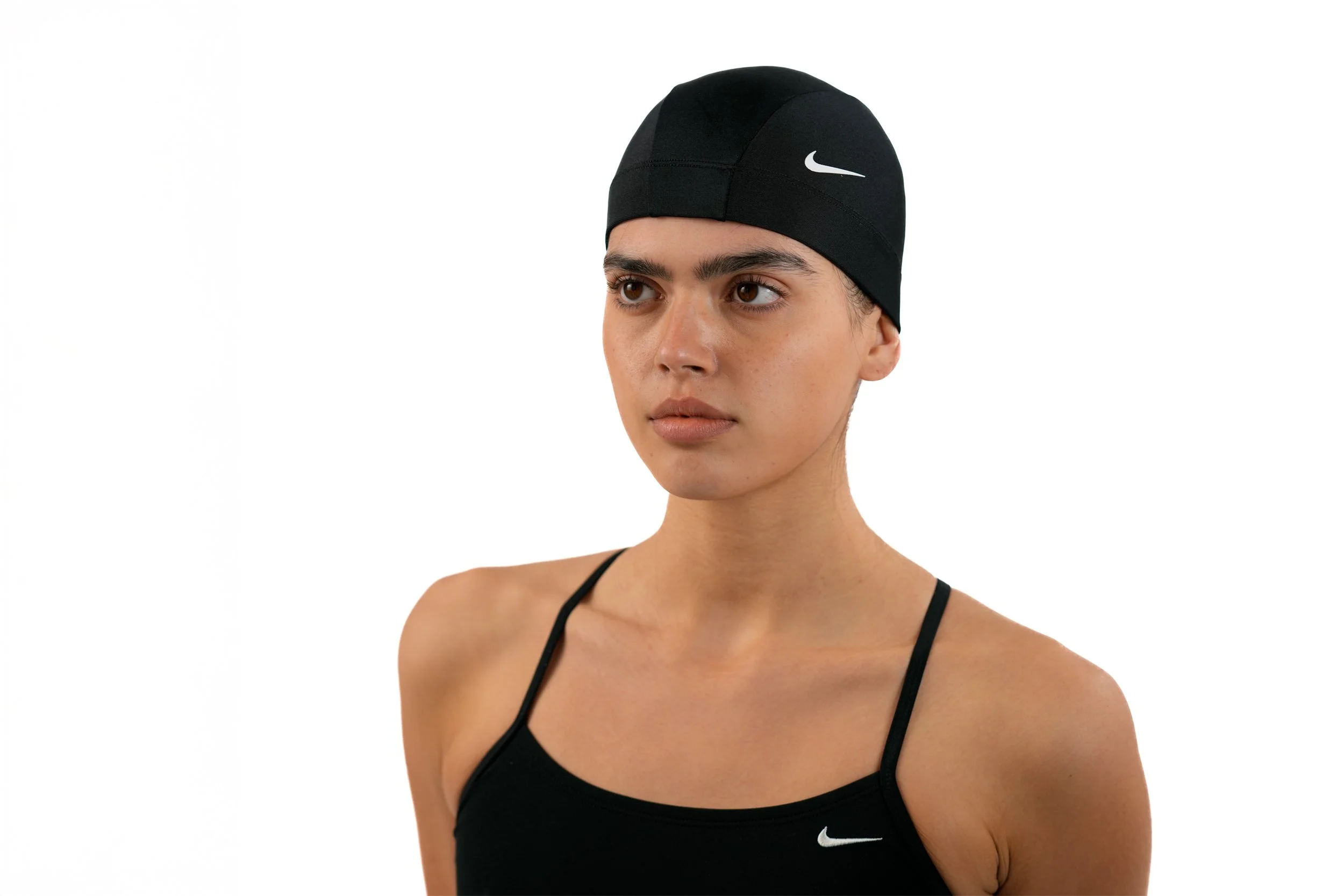 A woman in a black Nike swim cap and black sports top, looking to the side against a white background.