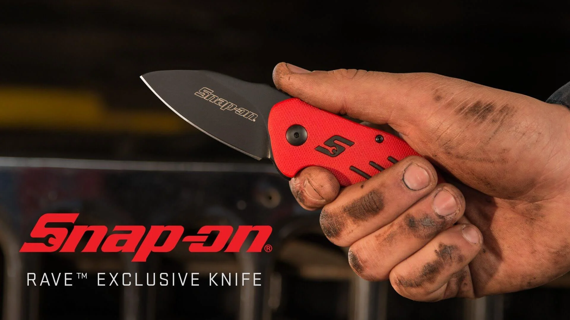 Close-up of a dirty, calloused hand holding a red and black Snap-on Rave exclusive folding pocket knife with the blade partially open, displaying the Snap-on logo on the blade.