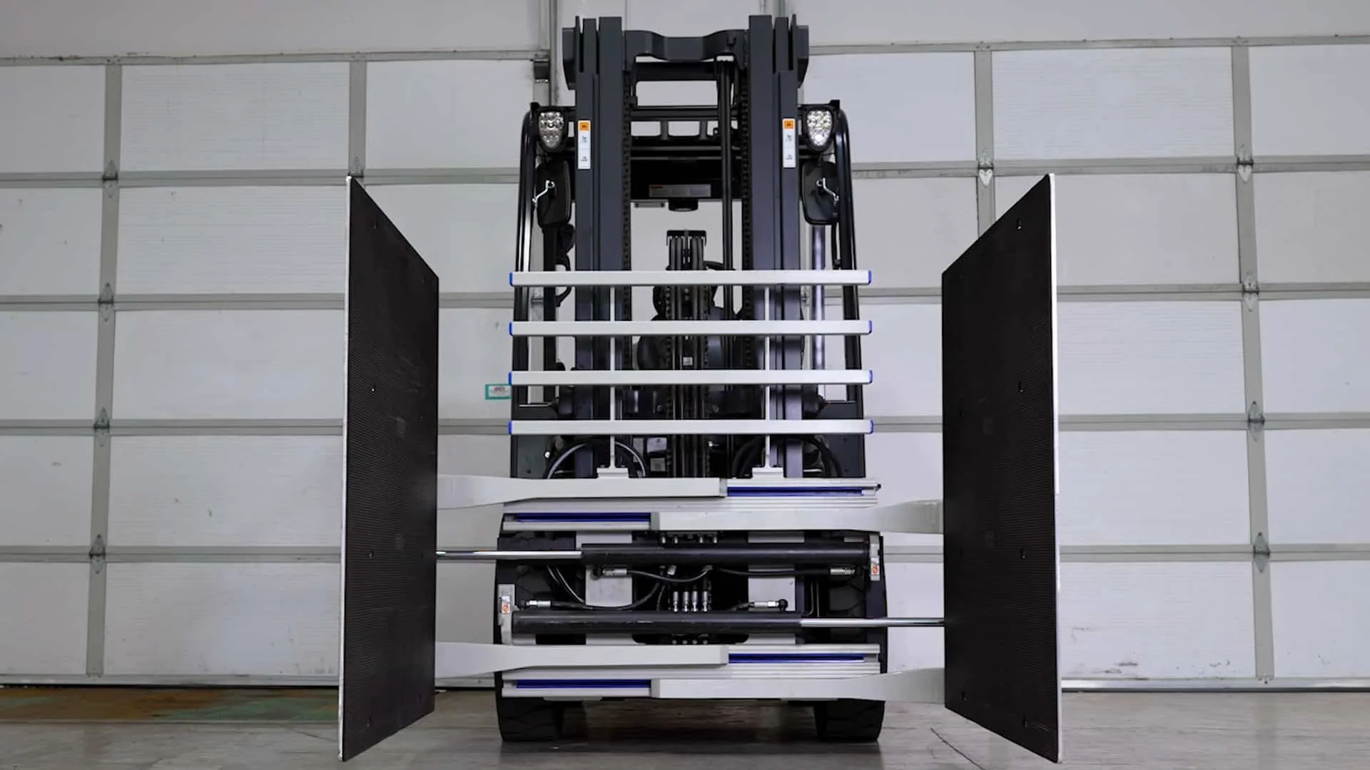 A black industrial forklift with open side panels, positioned against a white garage door.