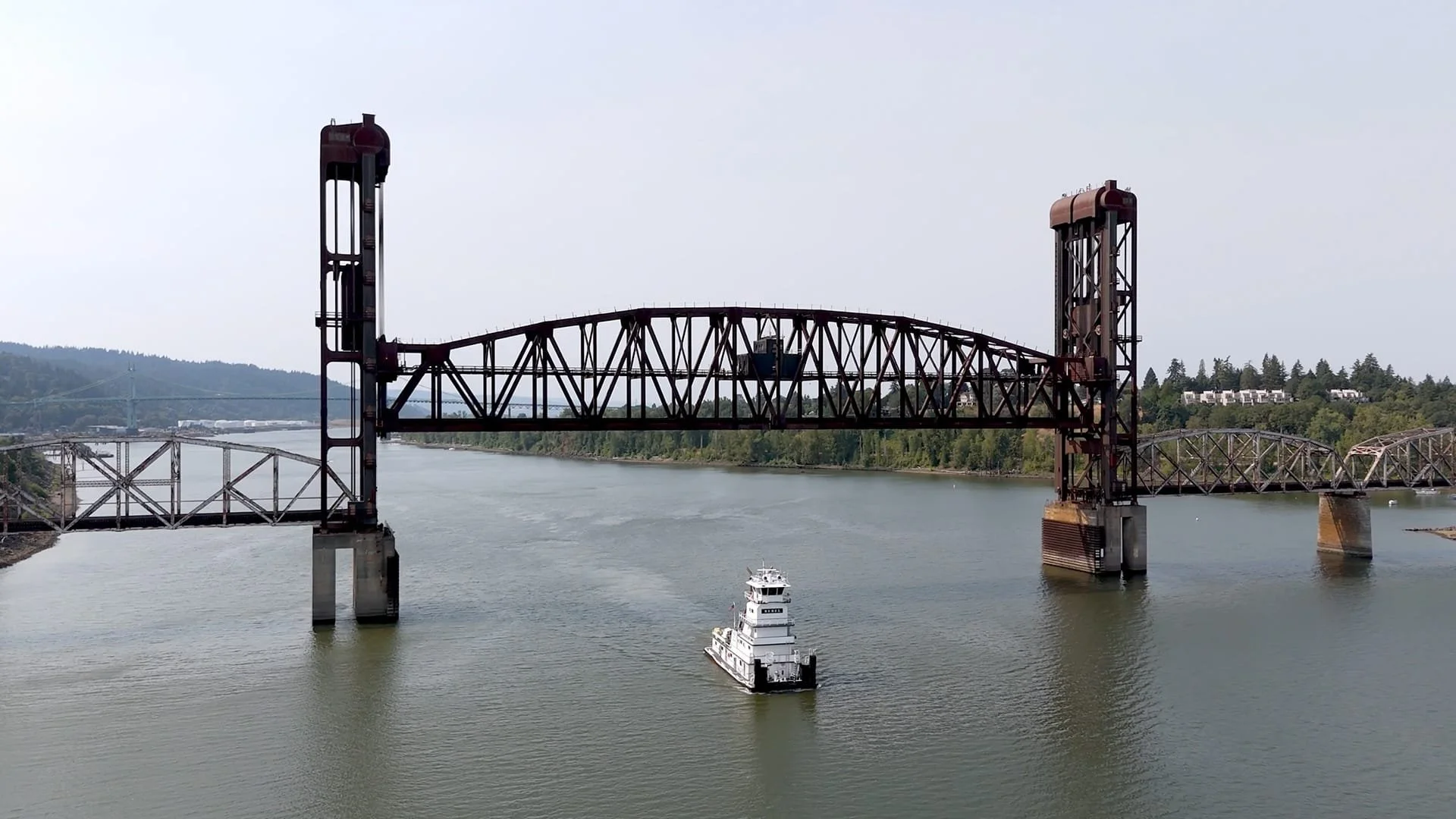 A large, rust-colored vertical lift bridge crossing a river with a white cruise ship passing underneath.