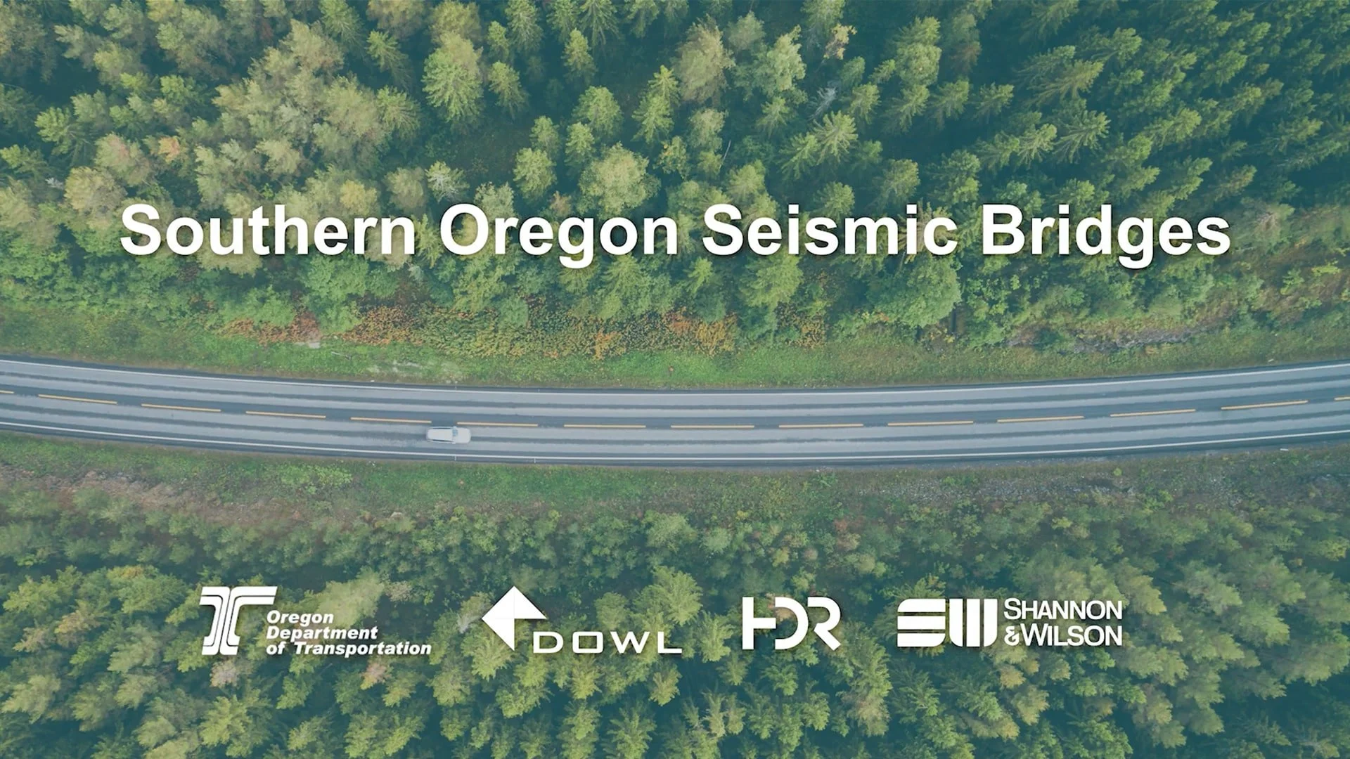 Aerial view of a highway cutting through a dense forest with green trees, with the text 'Southern Oregon Seismic Bridges' overlaid.