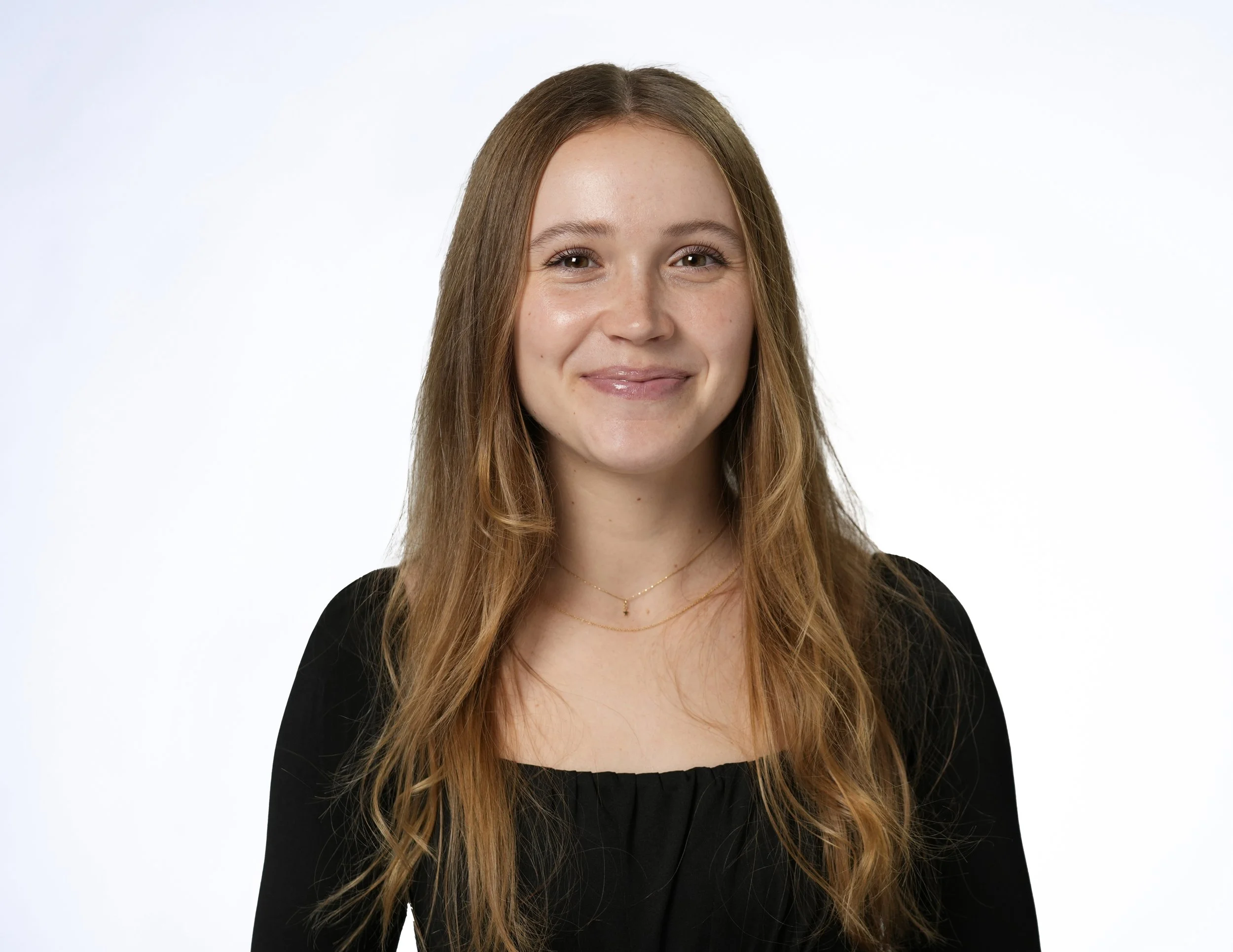 Portrait of a young woman with long reddish-brown hair, smiling slightly, against a plain white background.