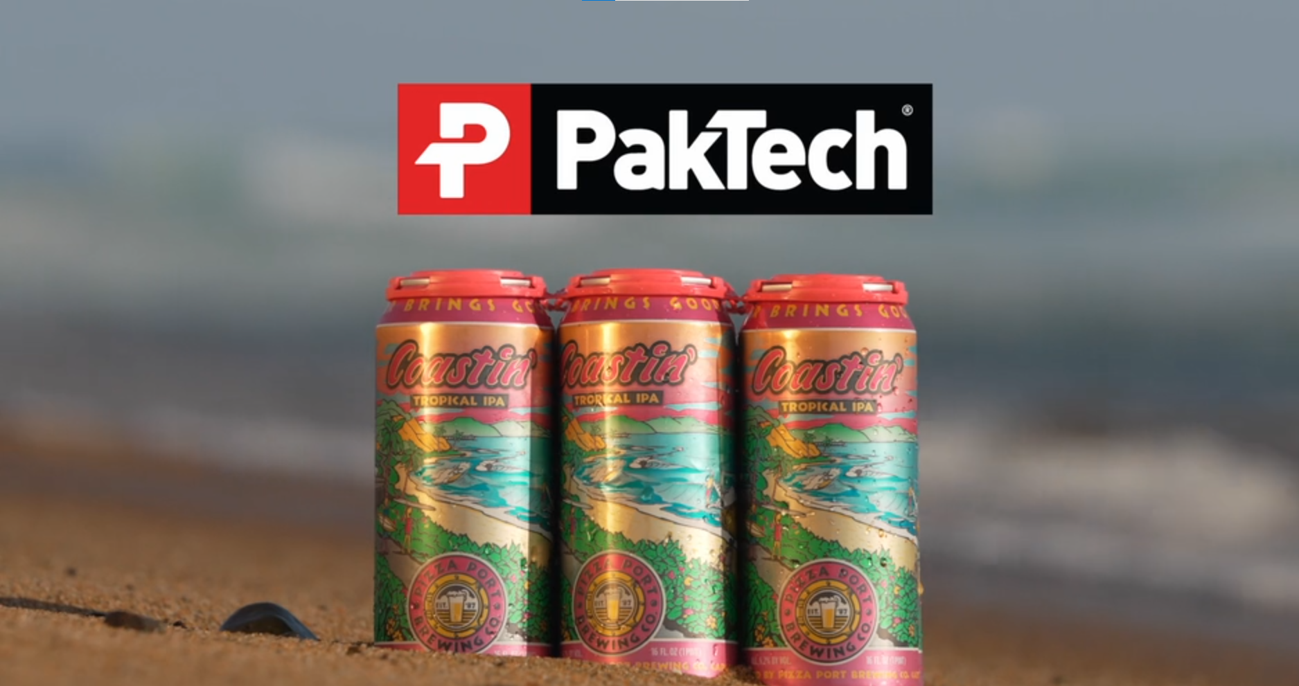 Three cans of Coastin Tropical IPA beer standing upright on a sandy surface with a beach and ocean in the background. A PakTech logo is visible above the cans.
