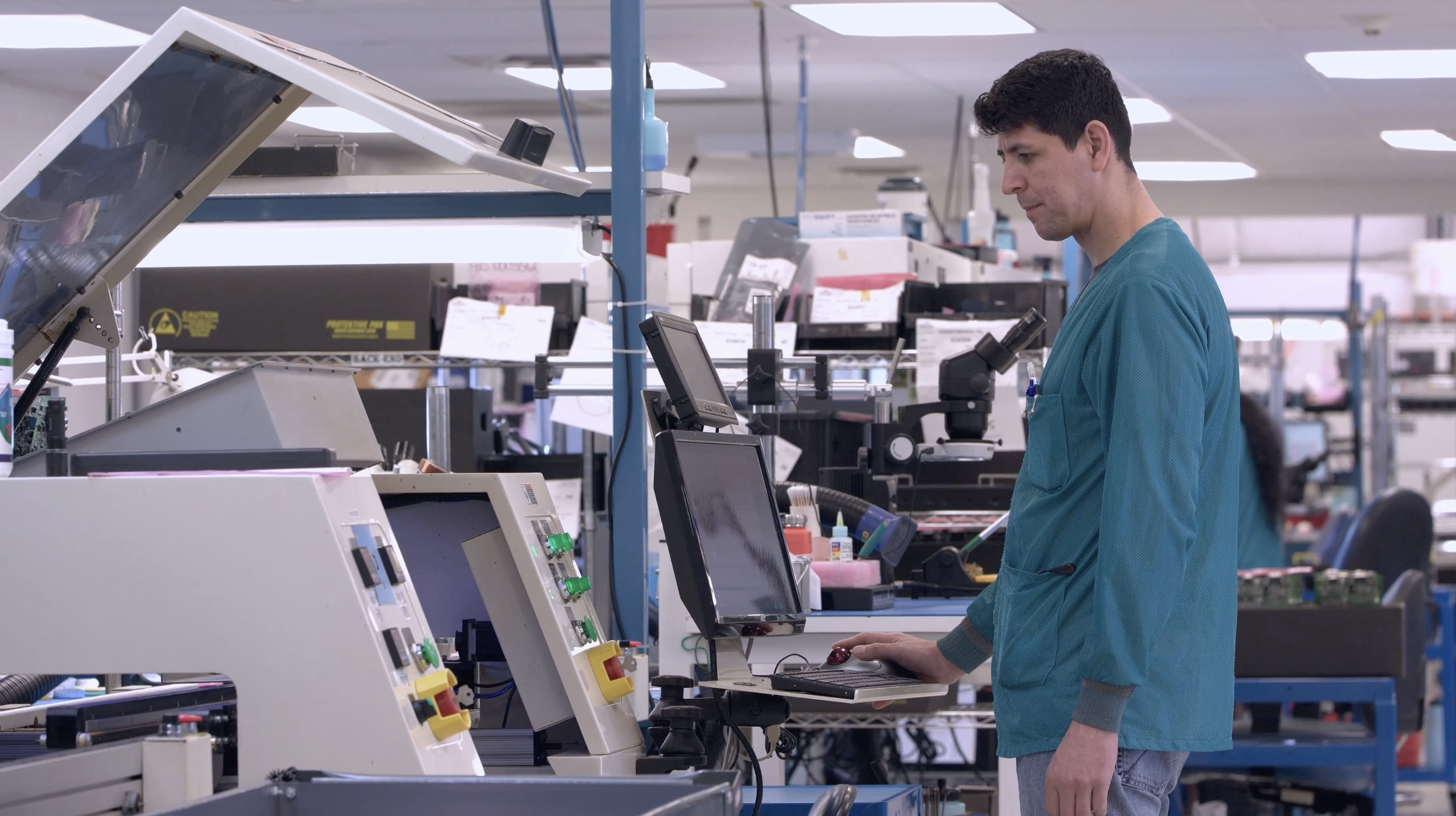 Factory worker in protective clothing operating industrial machinery and a computer control panel on a manufacturing floor