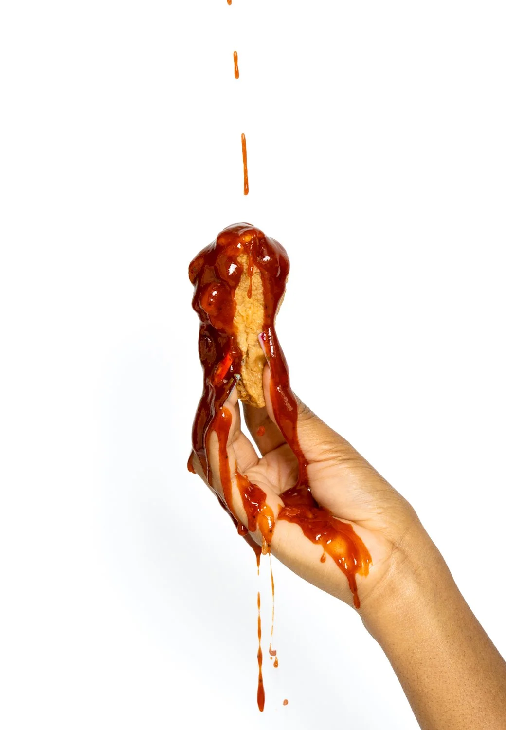 A hand holding a fried chicken tender covered in ketchup, with ketchup dripping from above