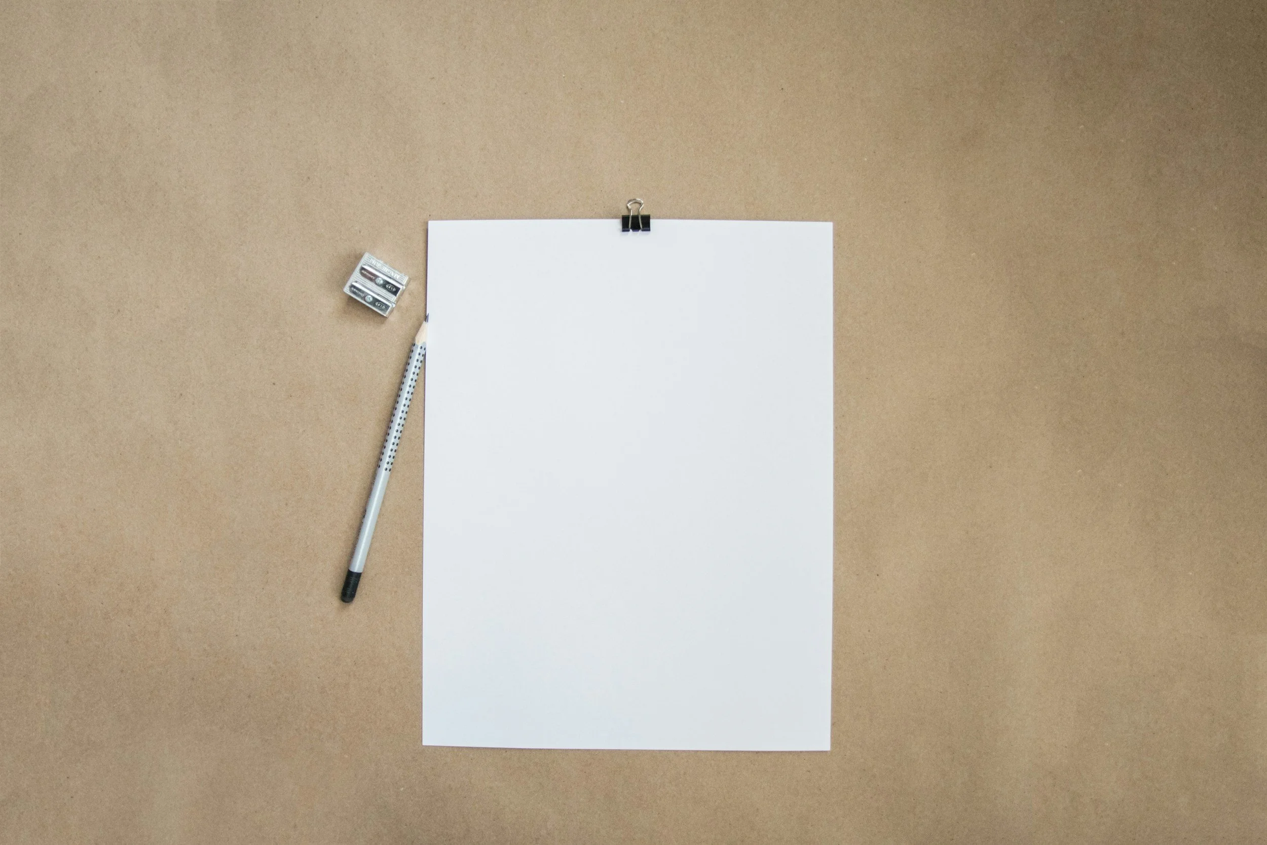 Blank white sheet of paper clipped to cork board with a black clip, a dotted black and white marker to the left, and two AA batteries nearby.